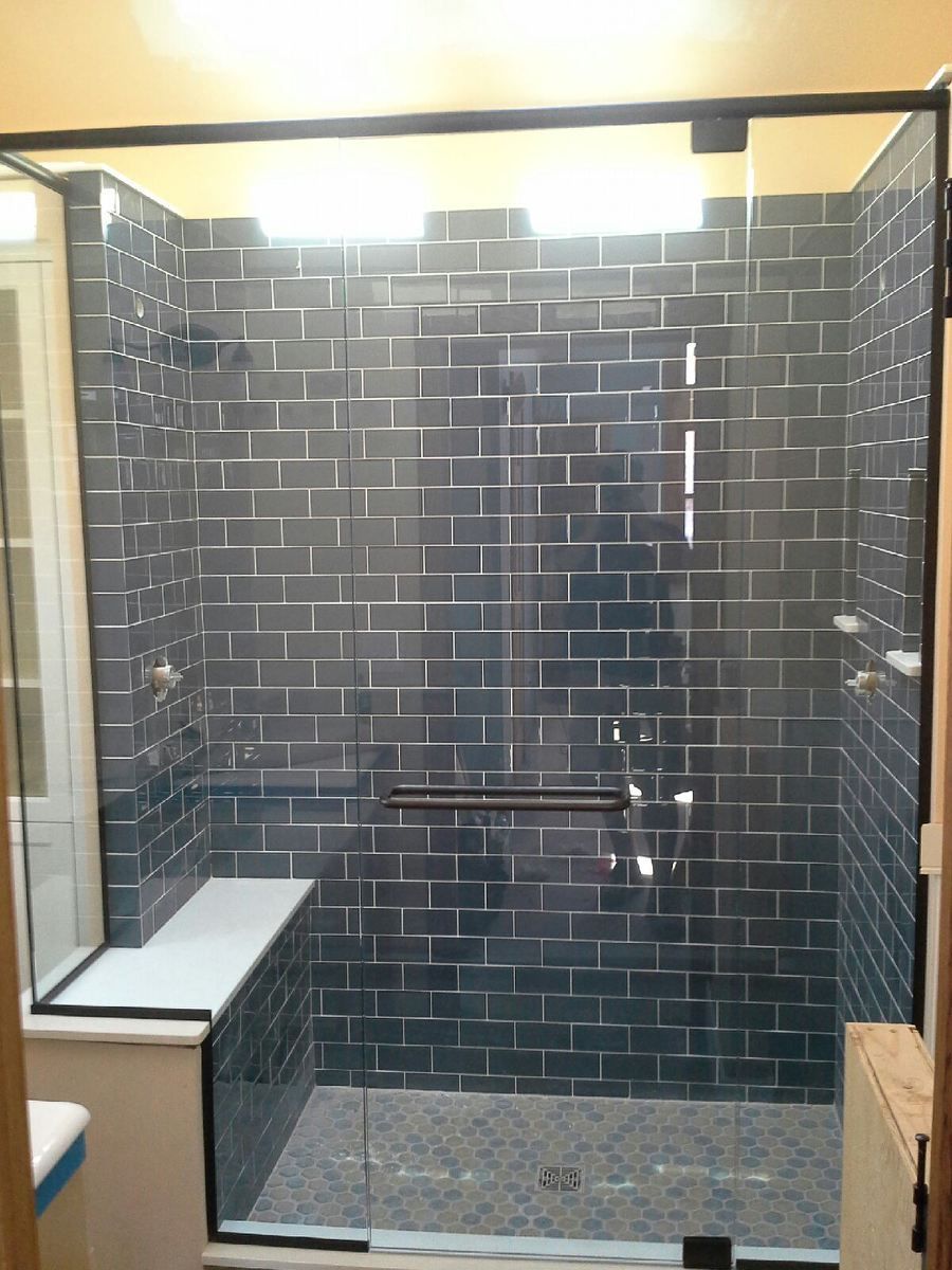 Modern bathroom with dark tiled walk-in shower and glass door, bench, and floor drain.