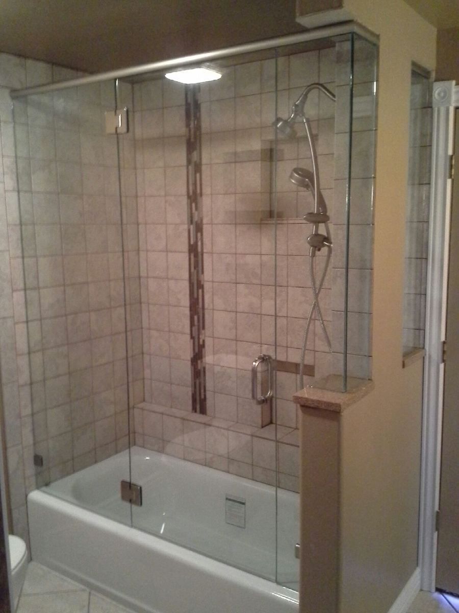 Glass-enclosed bathtub shower with beige tile walls and chrome fixtures