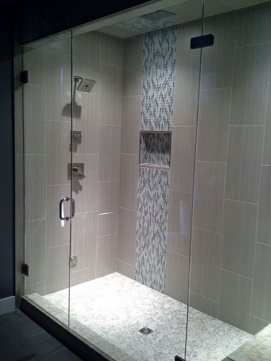 Modern glass shower stall with tiled walls, white floor, and a built-in shelf niche