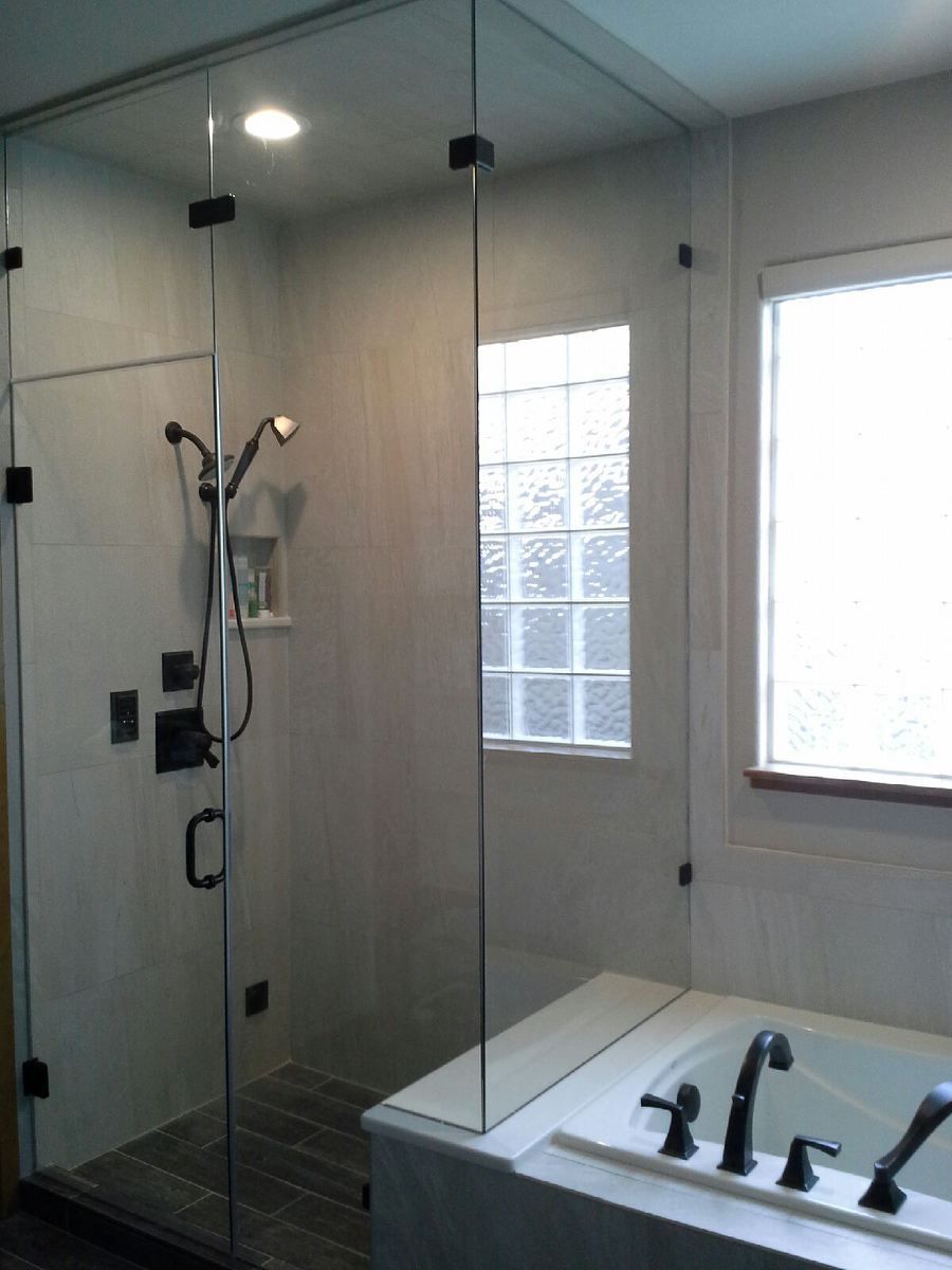 Glass-enclosed shower with handheld showerhead and window beside a bathtub faucet