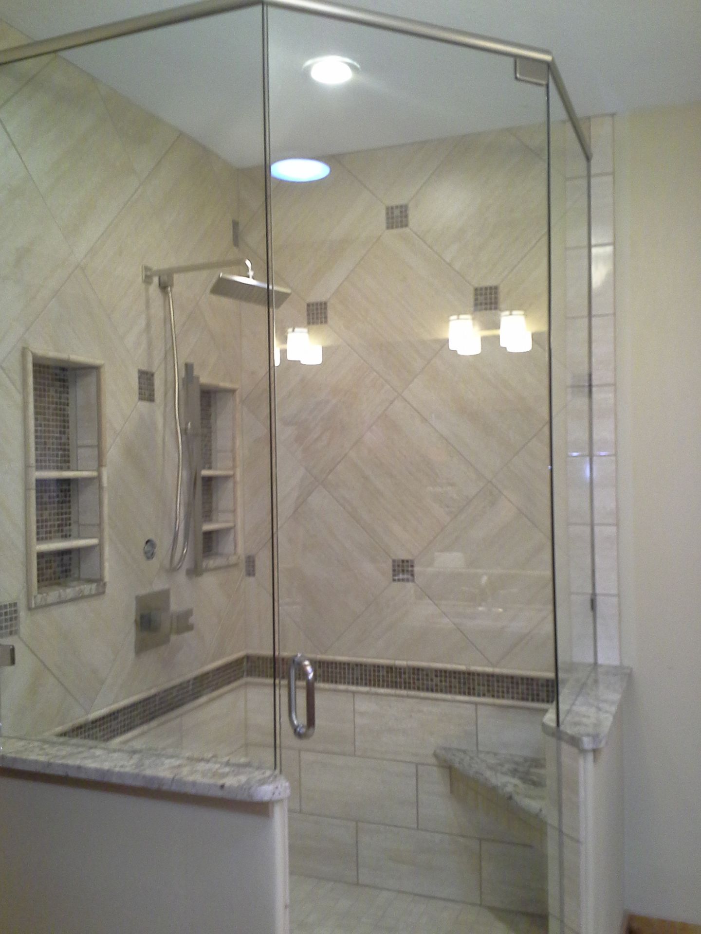 Glass-enclosed corner shower with beige tile walls, built-in niche, and chrome fixtures