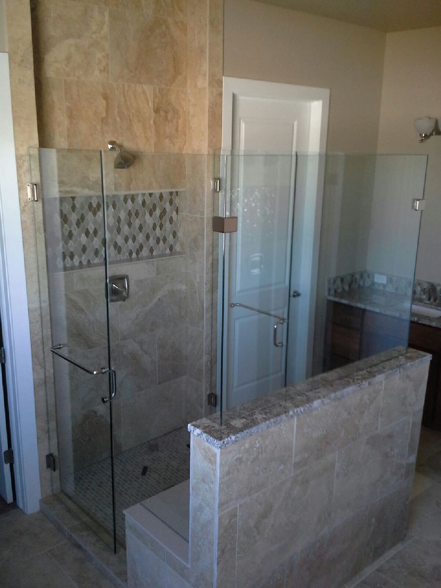 Modern walk-in shower with glass doors, beige tile, and a half-wall divider.