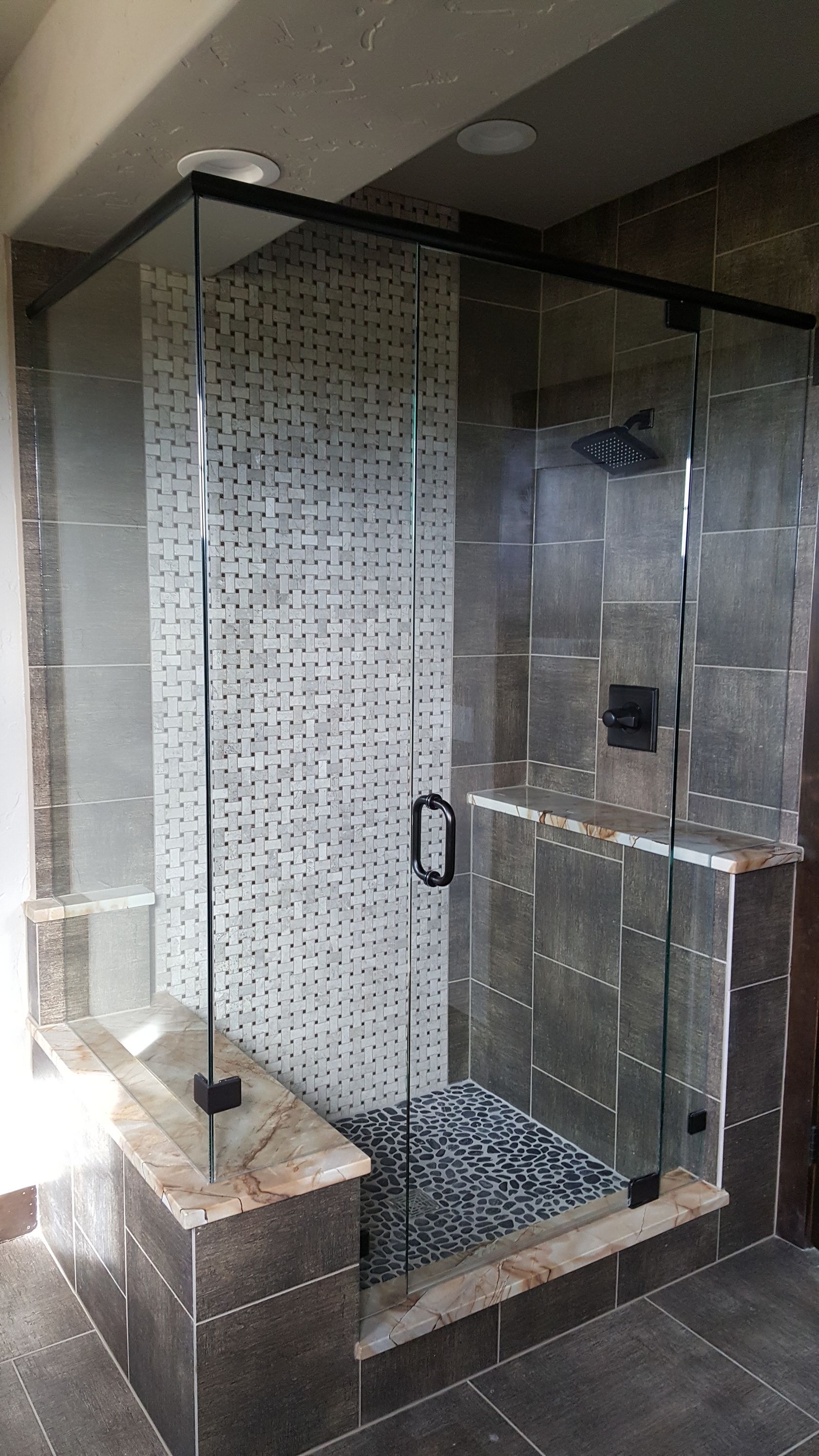 Glass shower enclosure with black frame, patterned tile wall, and brown tiled floor in a bathroom