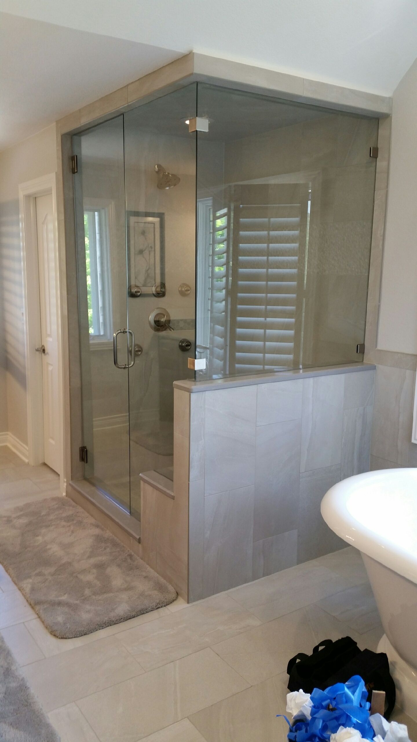 Modern bathroom with a glass shower enclosure, tiled half-wall, and beige floor; sink edge visible.