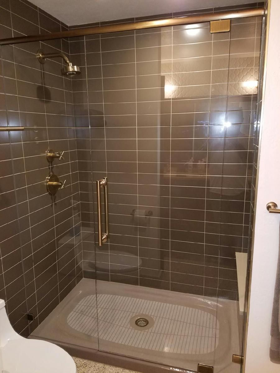 Modern tiled shower with glass door, white base, and chrome grab bar.
