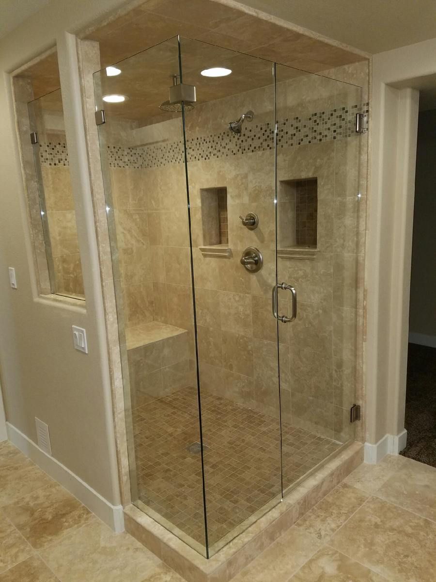 Glass-enclosed corner shower with beige tile and chrome fixtures in a bathroom