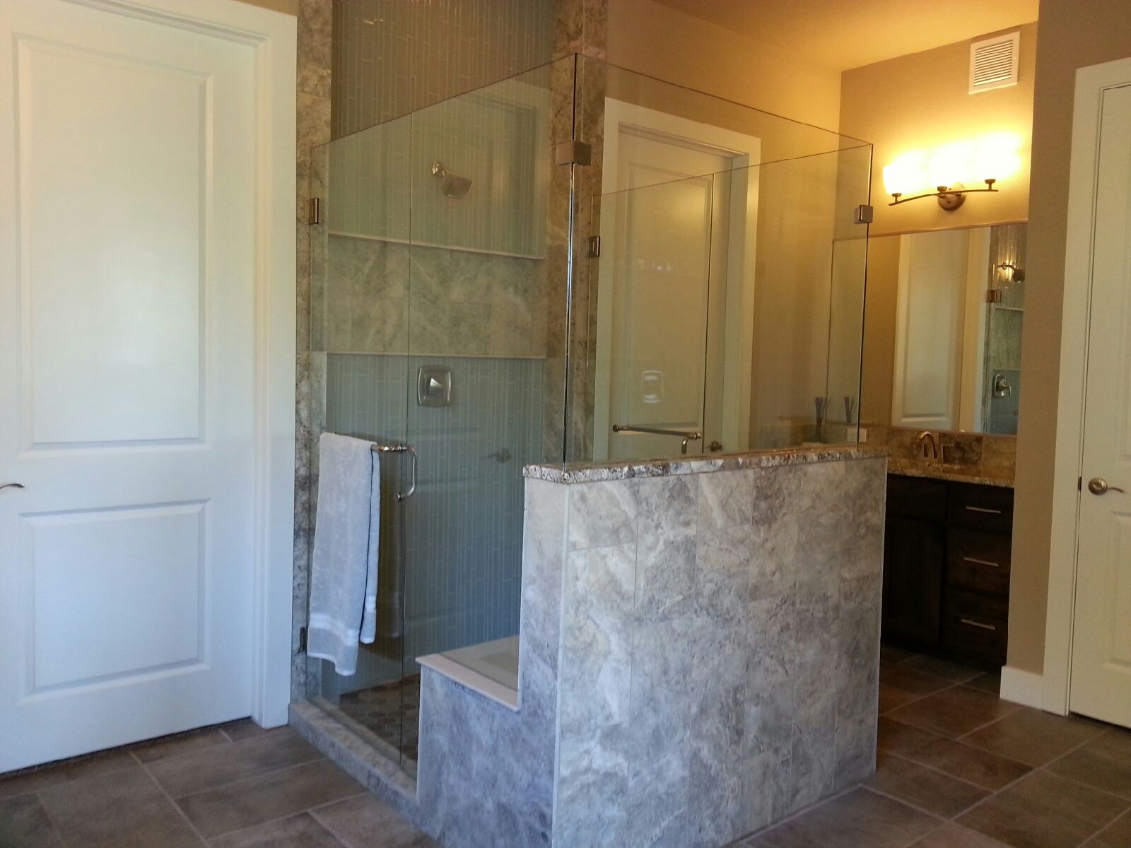 Modern bathroom with glass shower, stone vanity, wall sconce, and beige tile accents.