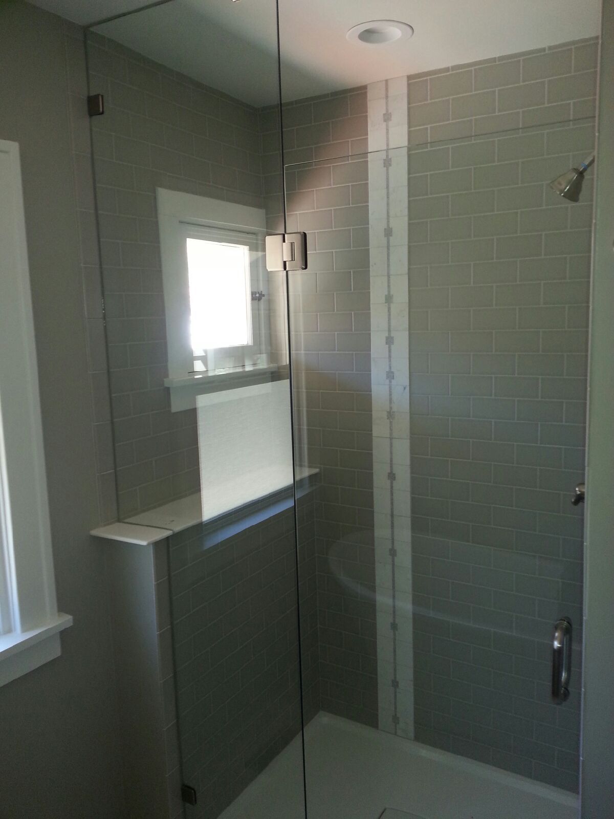 Small bathroom with a glass shower enclosure, white tile walls, and a window.