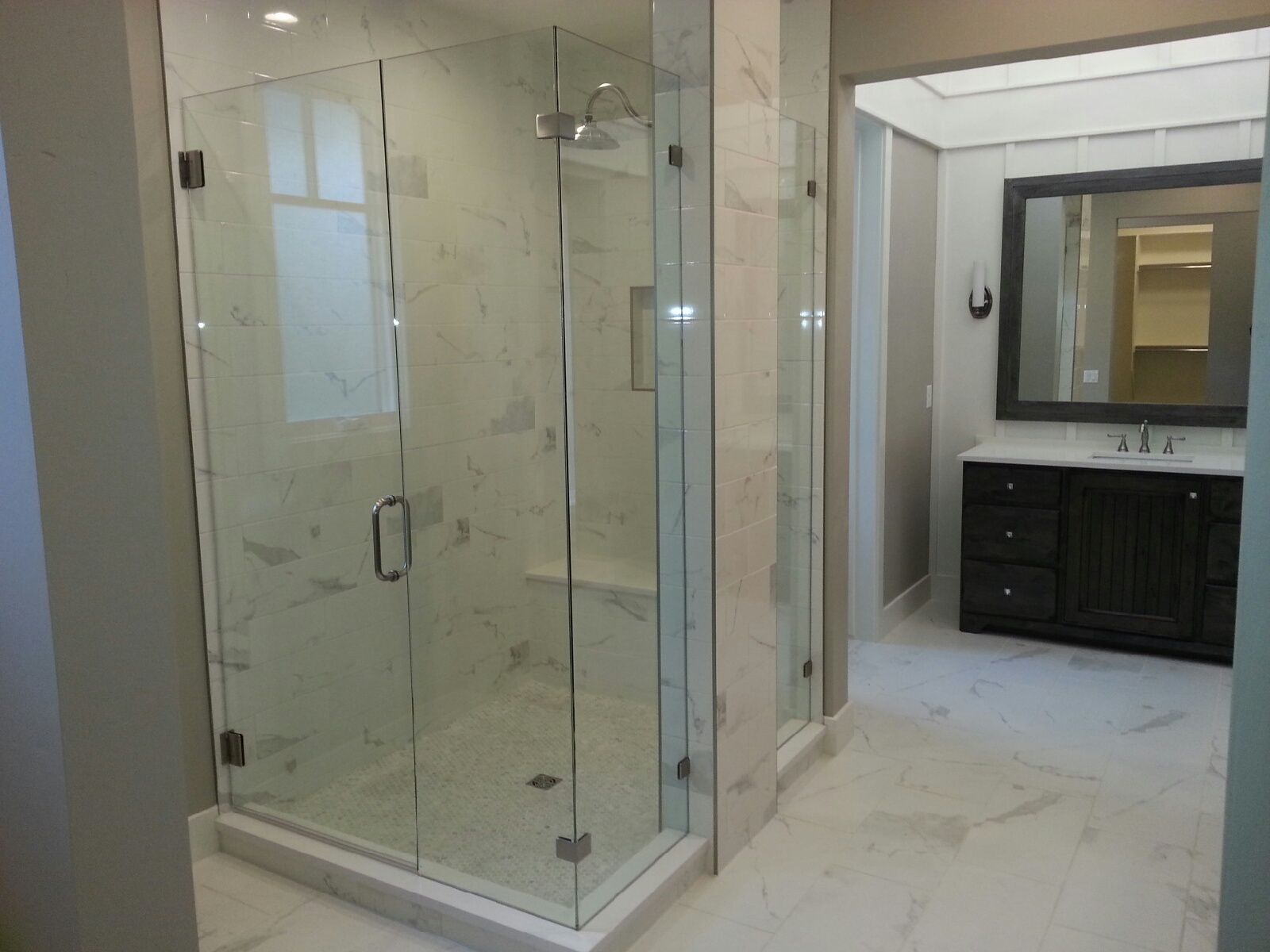 Modern bathroom with glass-enclosed shower, beige tile, and dark vanity sink area.