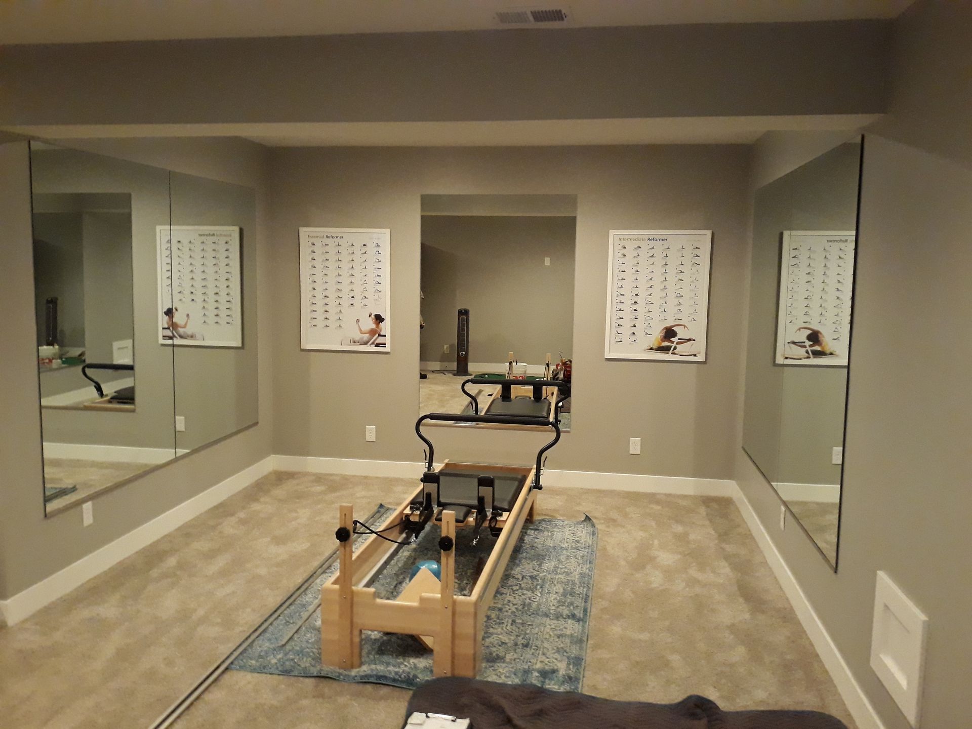 Home Pilates reformer in a mirrored exercise room with gray walls and beige carpet.
