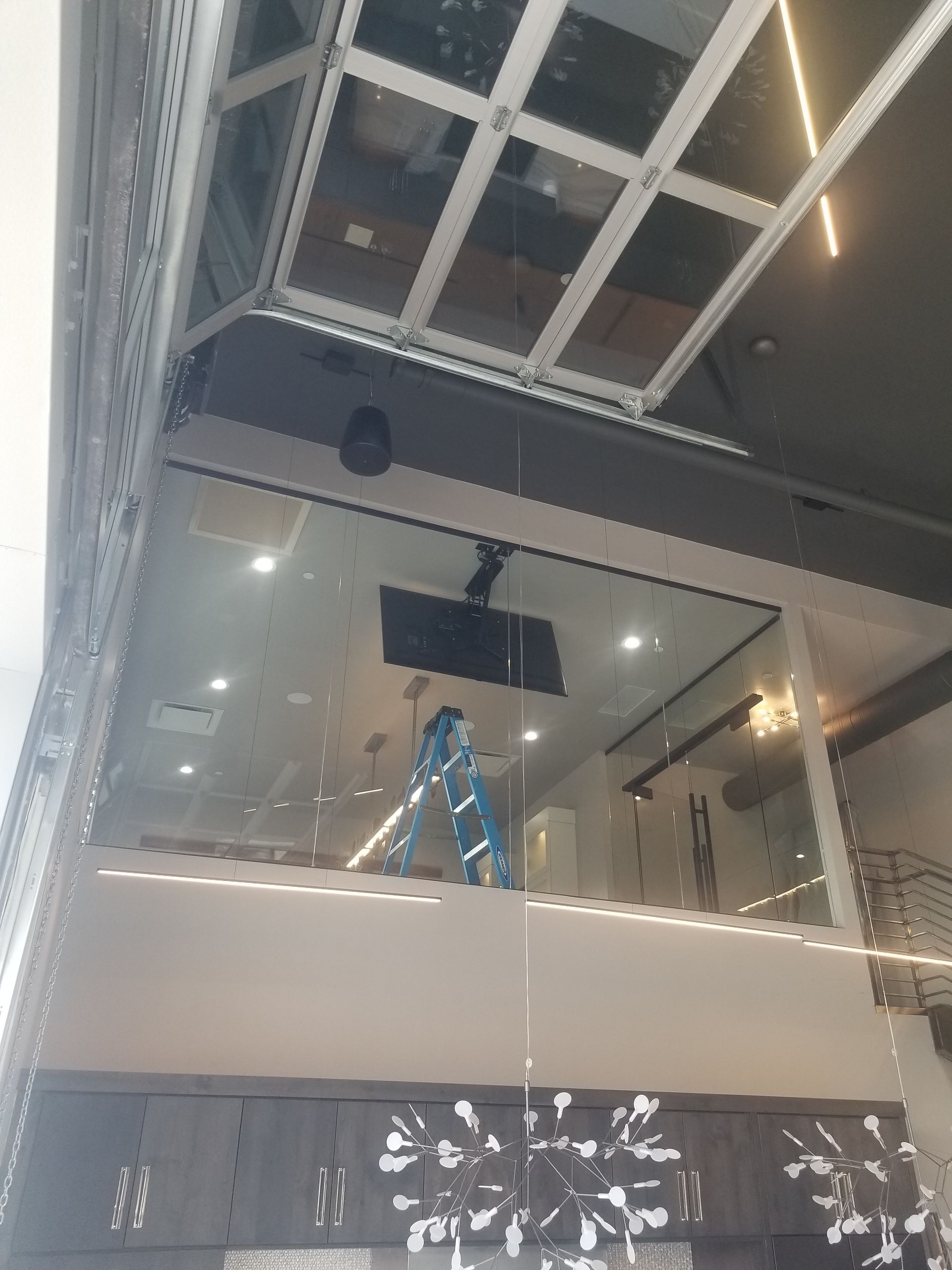 Person on a blue ladder working in a modern indoor atrium with a hanging light fixture