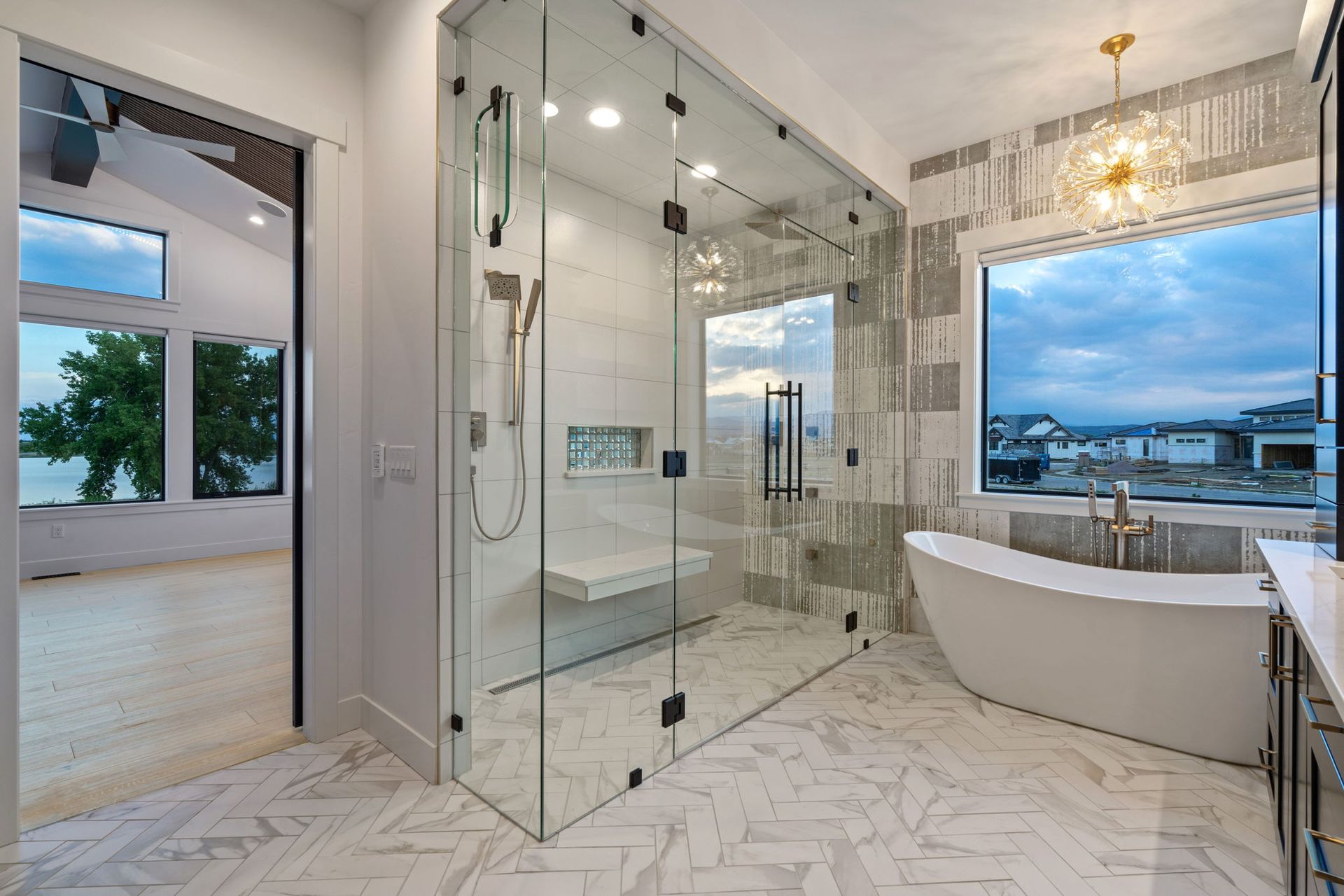 Modern bathroom with glass shower, freestanding tub, white marble tile, and large window view