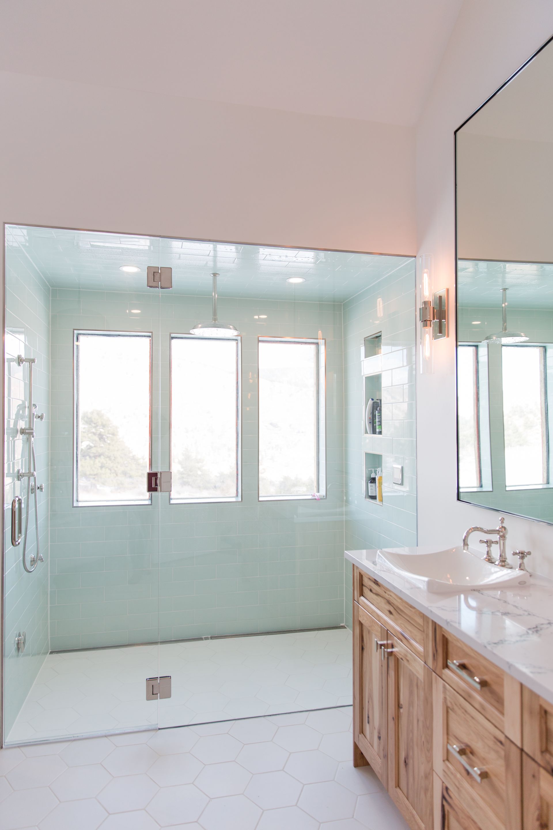 Bright bathroom with mint-green walls, double vanity, large mirror, and windows by the shower area.