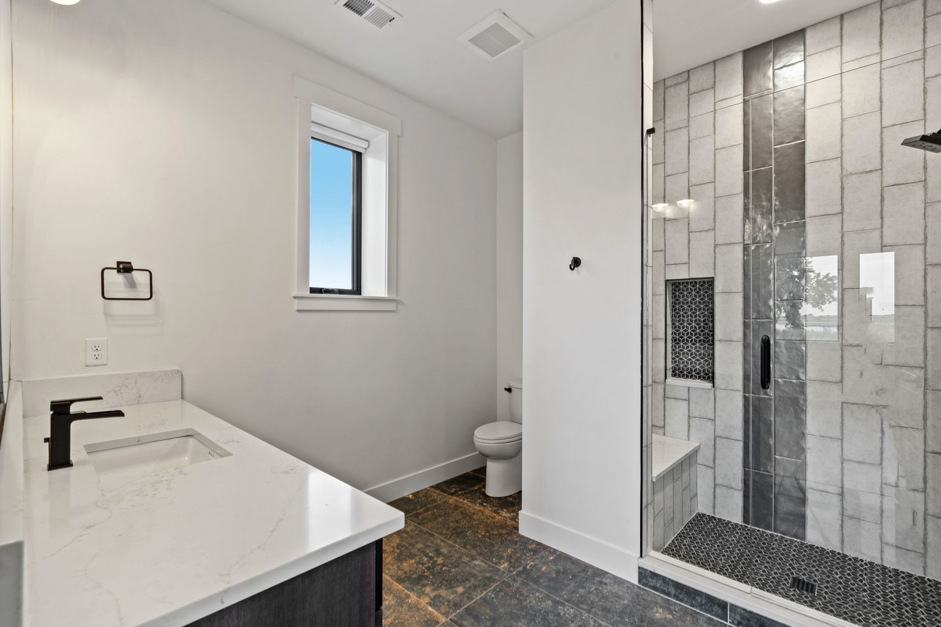 Modern bathroom with white vanity, small window, toilet, and glass-tiled shower.