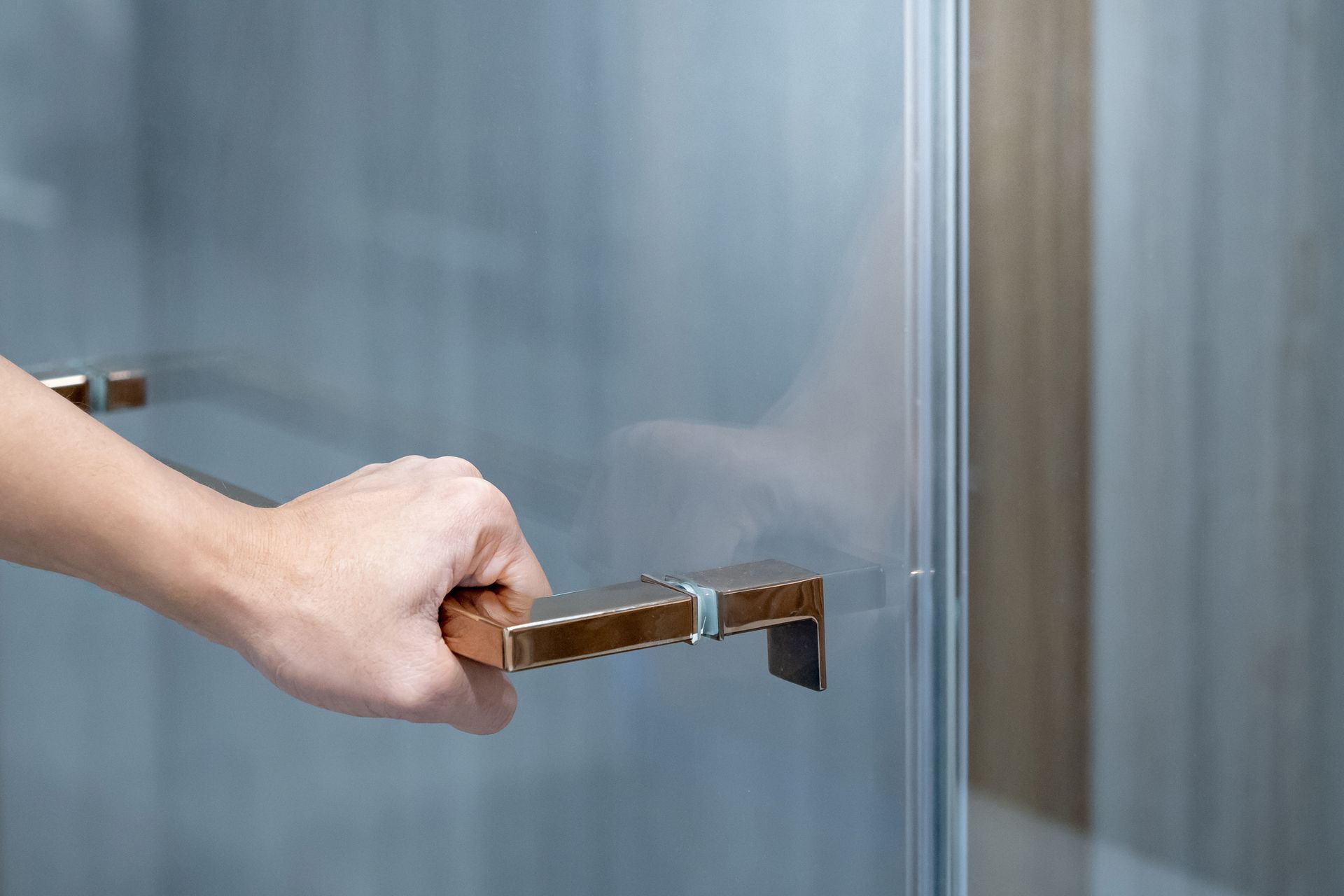 Hand opening a glass door with a metal handle