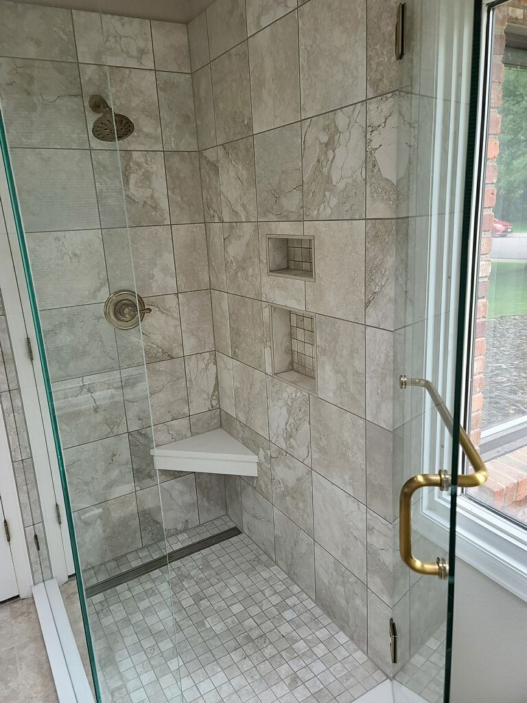 Small tiled shower with a built-in bench, grab bars, and glass door in a bathroom