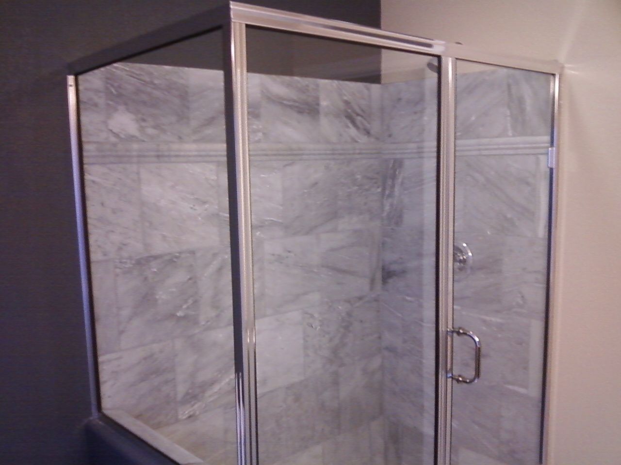 Glass-framed shower stall with gray tiled walls and a chrome handle