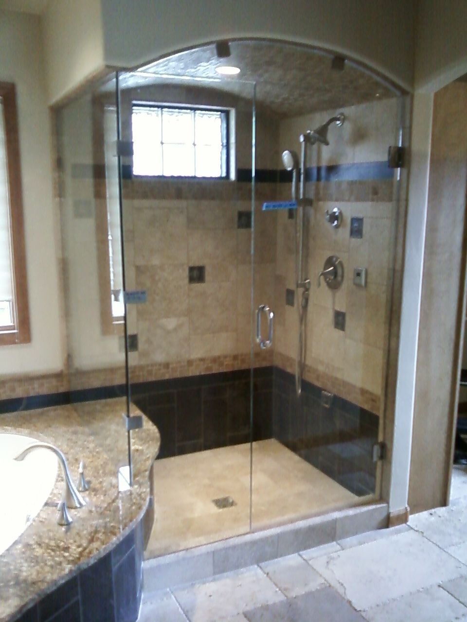 Glass walk-in shower with beige tile, dark bench, and chrome fixtures in a bathroom