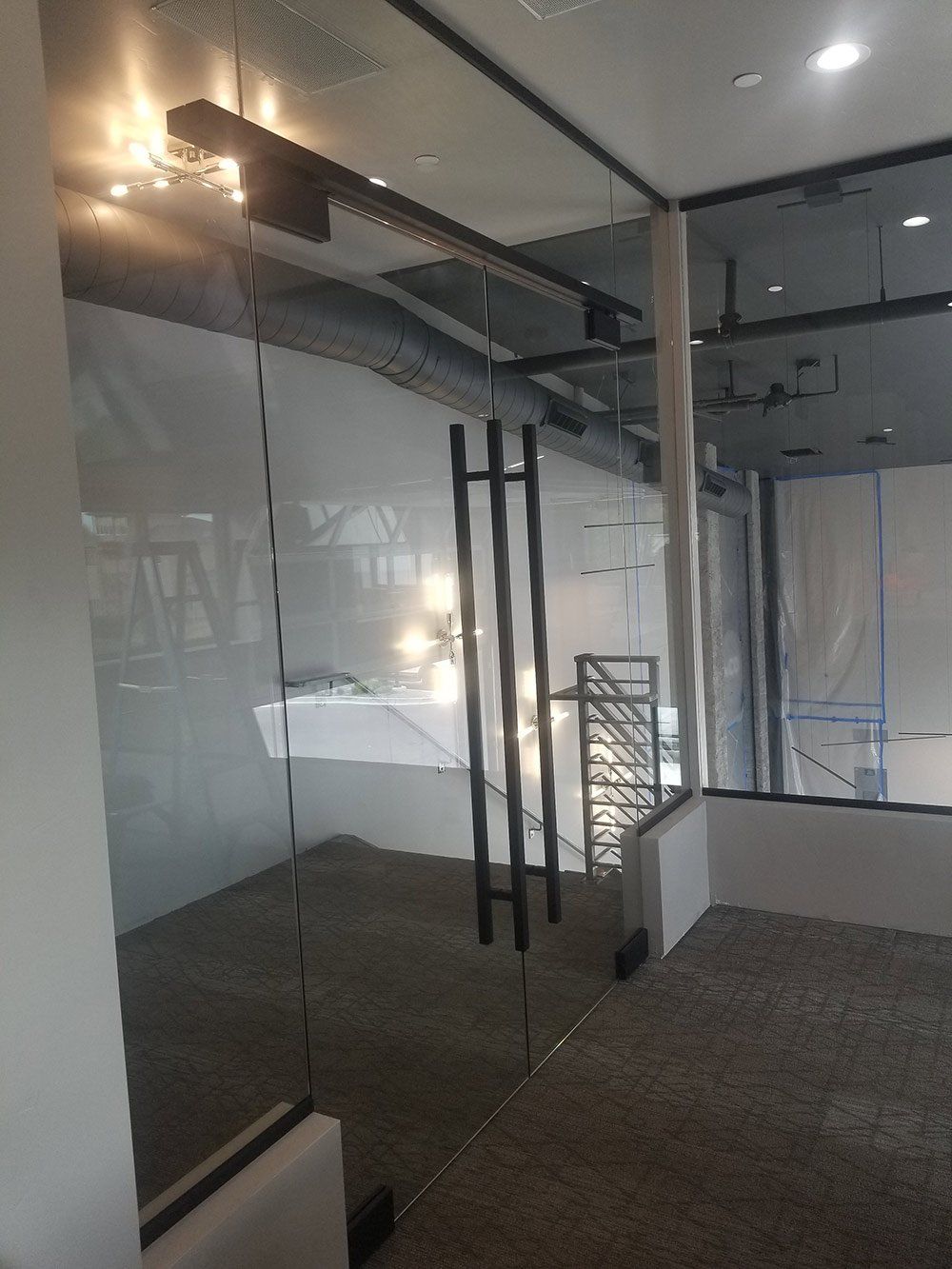 Modern office interior with glass walls, black-framed doors, and a patterned carpeted floor