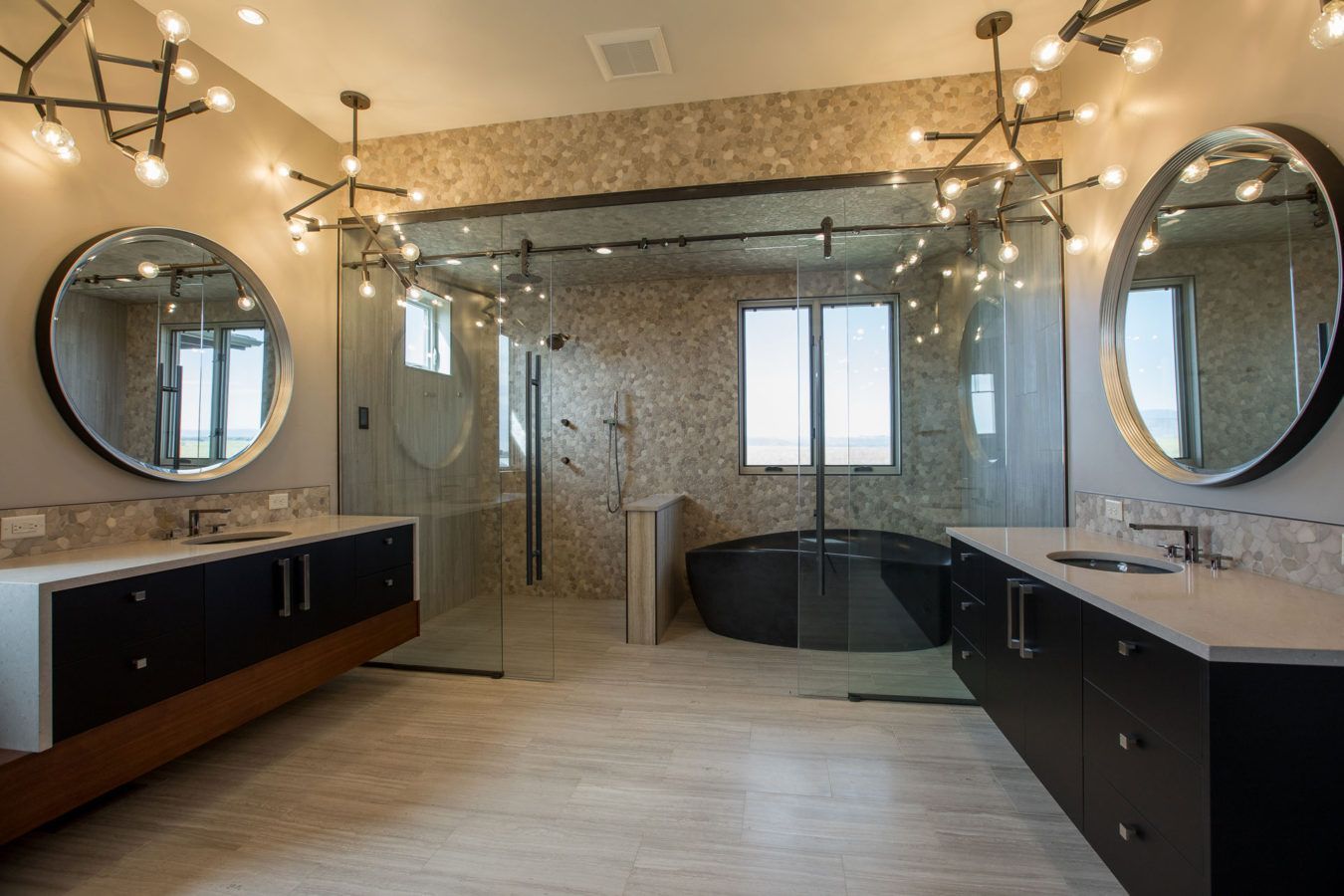 Luxury bathroom with dual round mirrors, double sinks, and a glass-enclosed shower and tub.