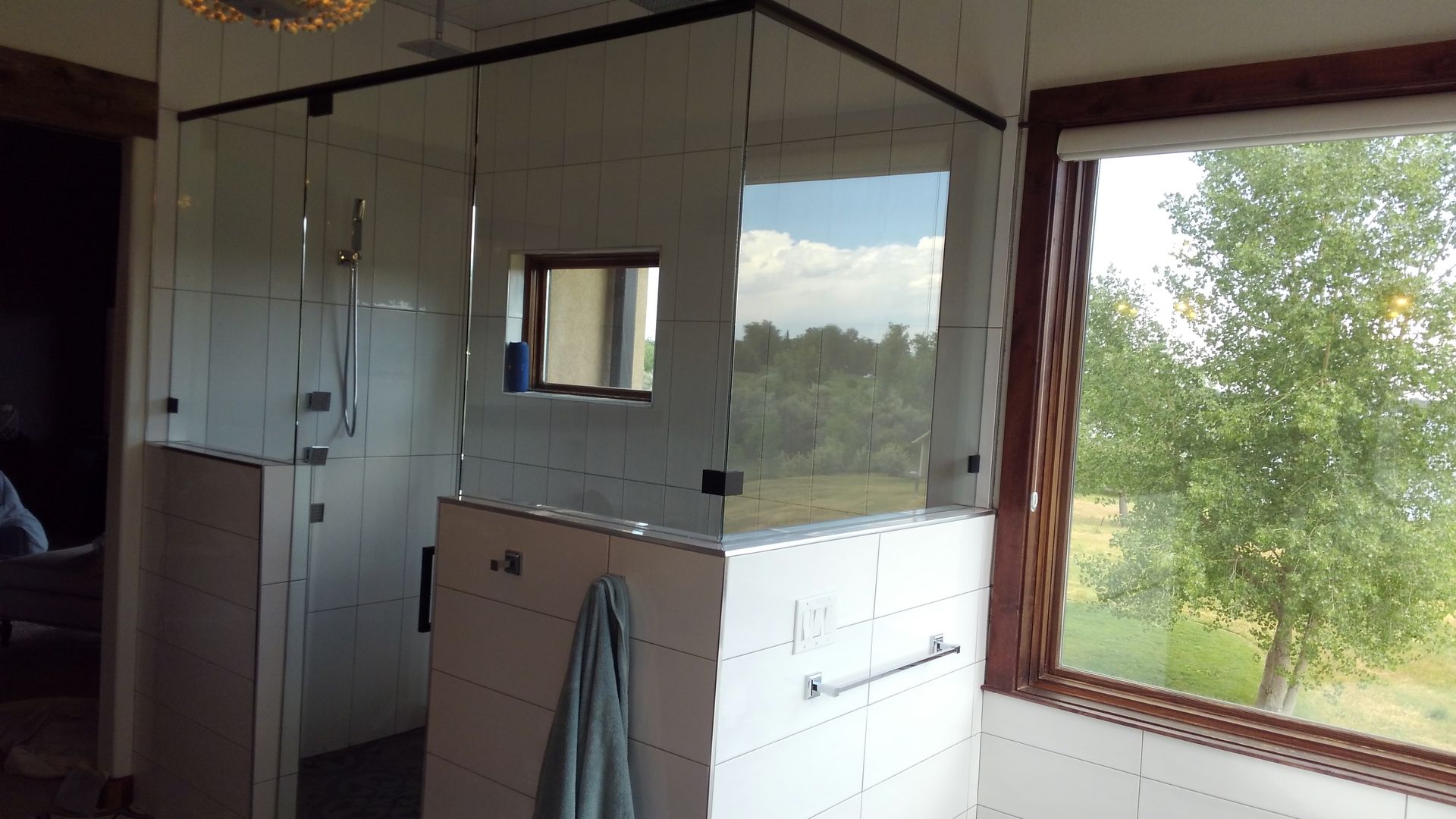 Bright bathroom with white tile, mirrored cabinets, and a large window looking out to trees and sky
