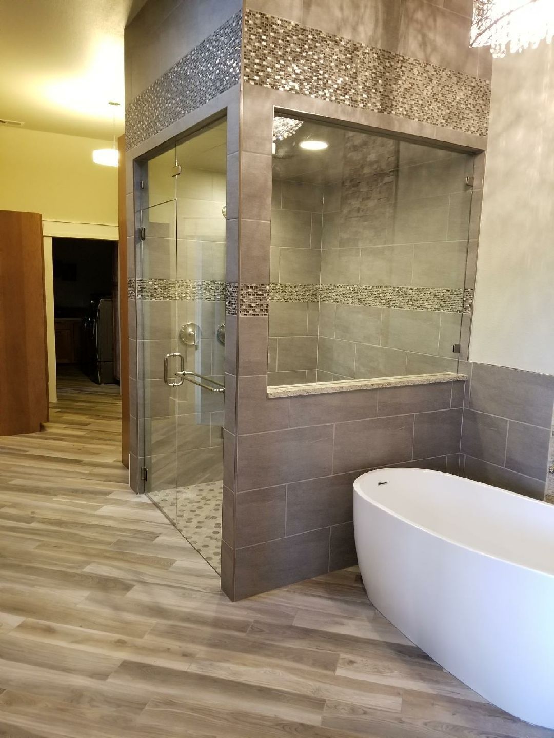Bathroom with glass shower enclosure and freestanding white tub on gray tiled floor