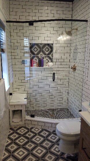 Small bathroom with white subway tiles, black-and-white patterned floor, shower, sink, and toilet.