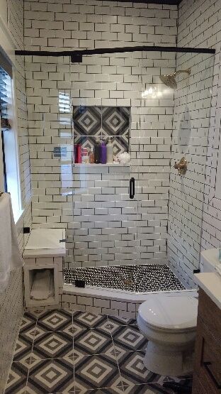Tiled bathroom with walk-in shower, white subway walls, patterned floor, vanity, and toilet