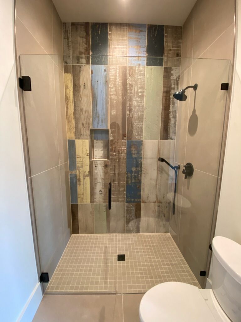 Modern glass shower with tiled mosaic wall and beige floor in a bathroom
