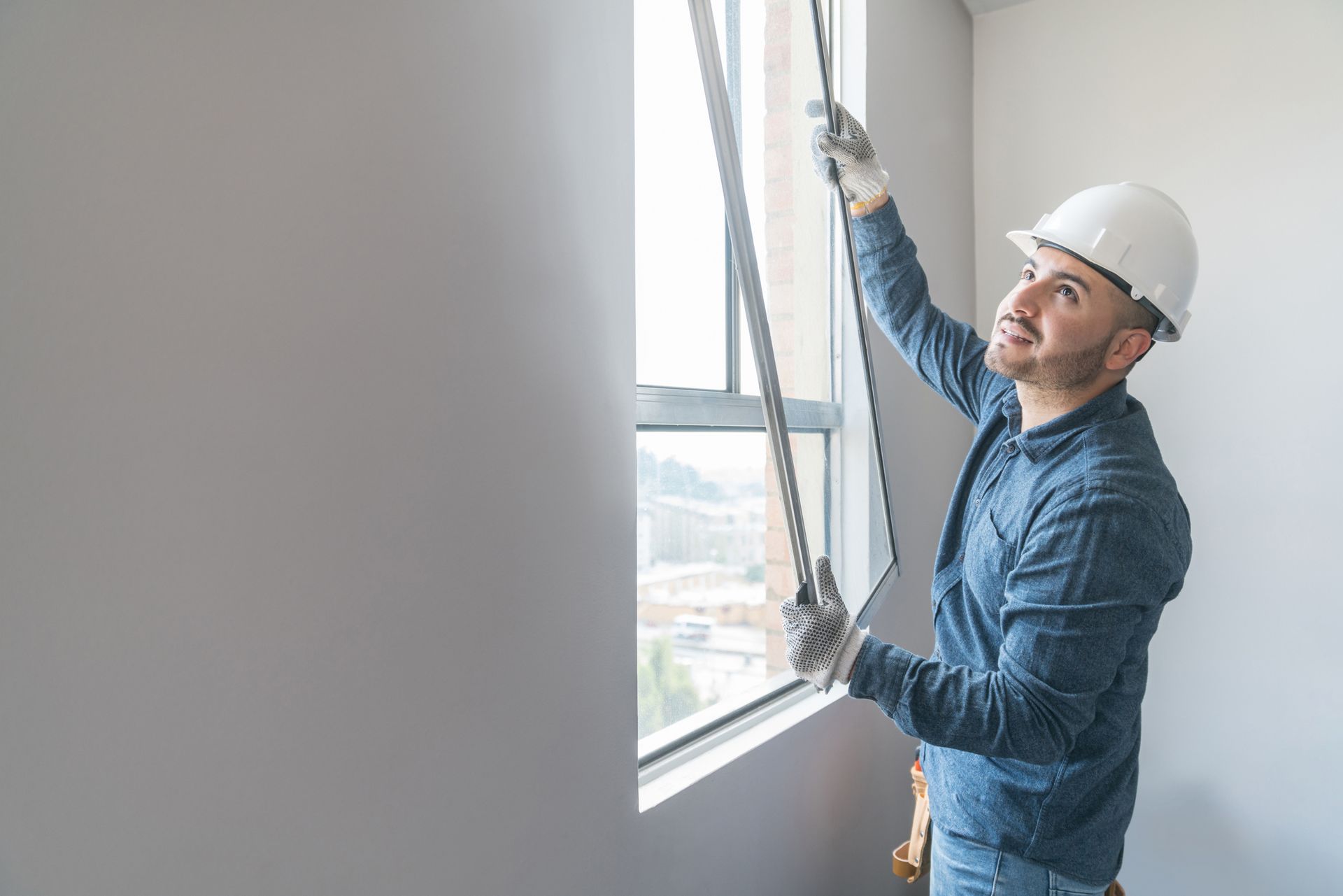 Building contractor installing a window at a house, highlighting professional glass repair and installation services. Worker in a hard hat installing a window blind beside a bright window