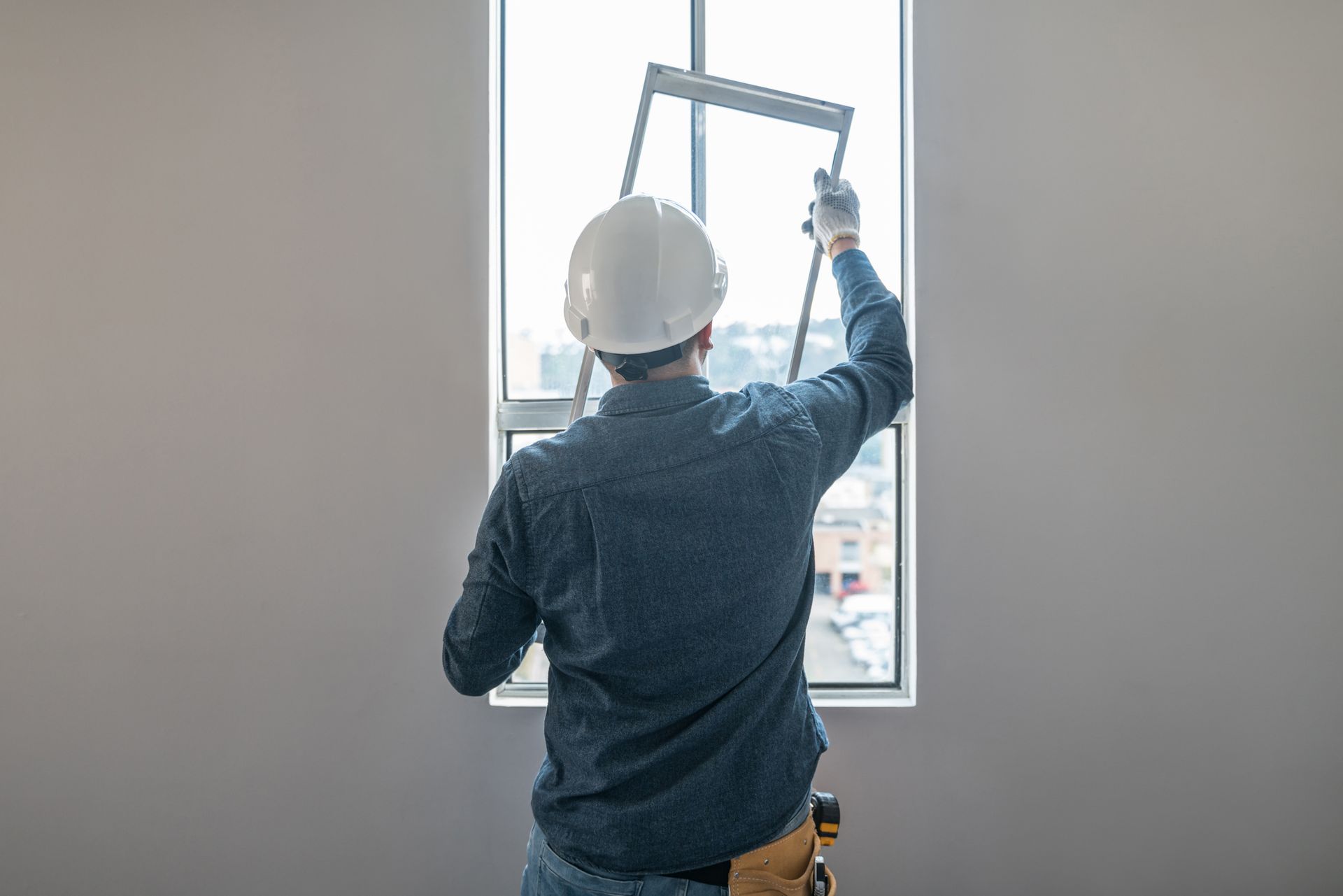 Constructor installing a window in a new building, highlighting professional window repair and installation services. Worker in a hard hat measuring a window opening inside a room under construction