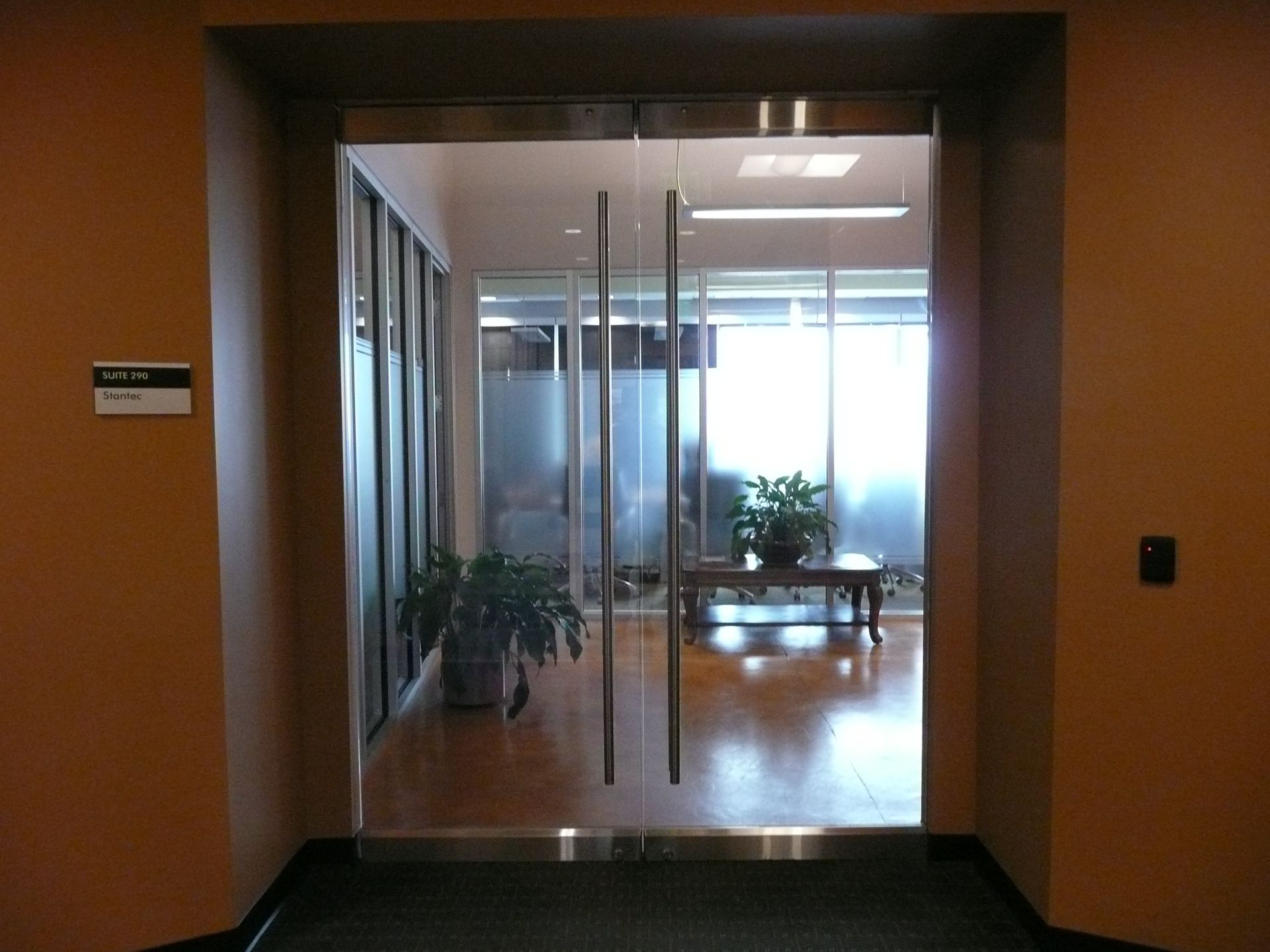 Glass office doorway opening into a bright conference room with wooden floors and potted plants