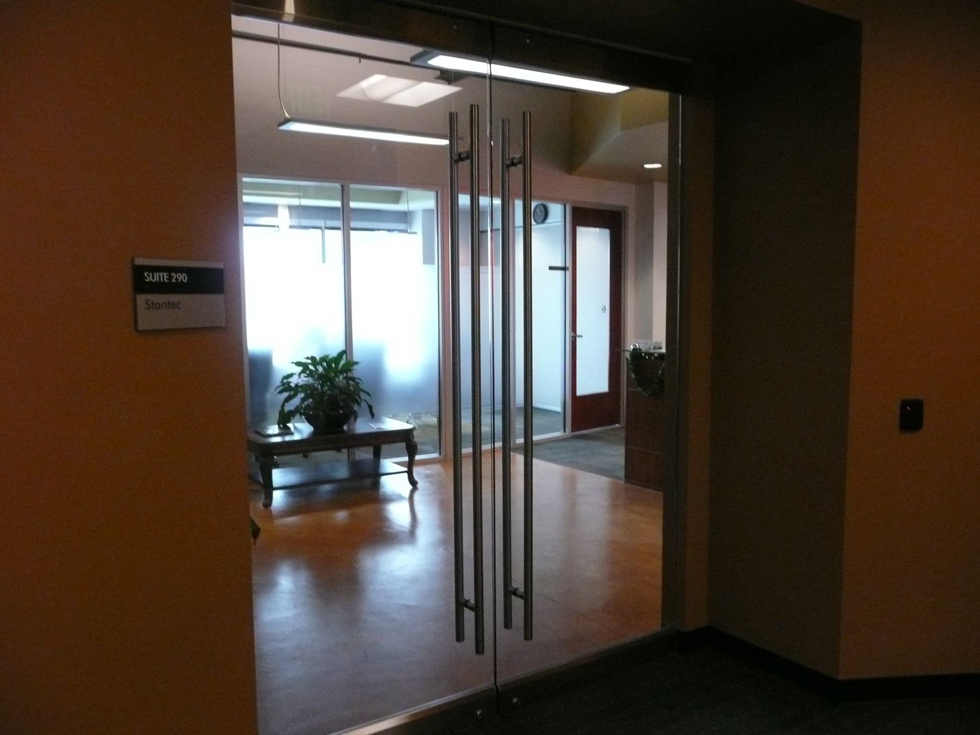 Glass office entrance with double doors, wood floor, and potted plants in a hallway