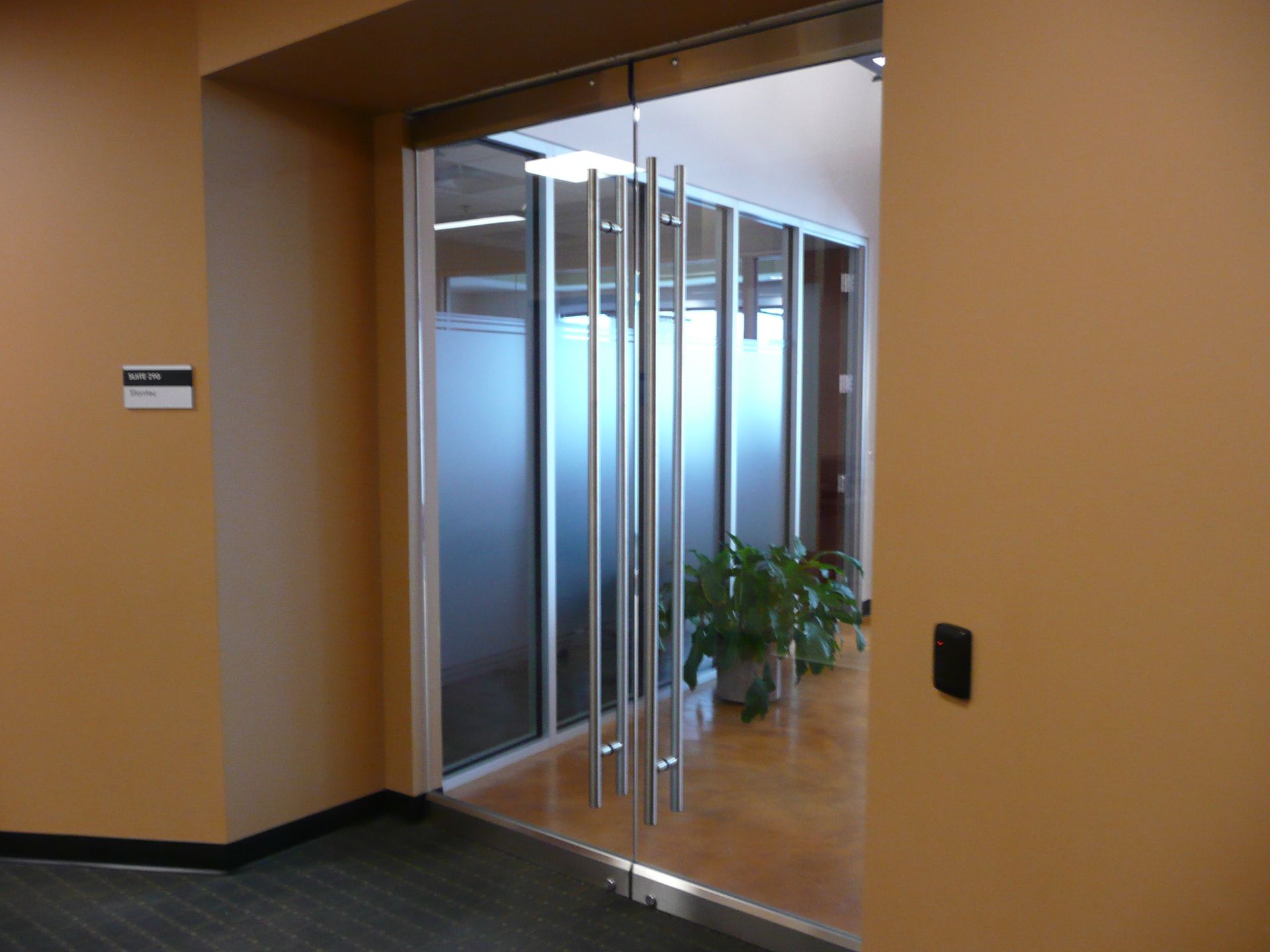 Glass-walled elevator lobby with potted plant in a beige hallway