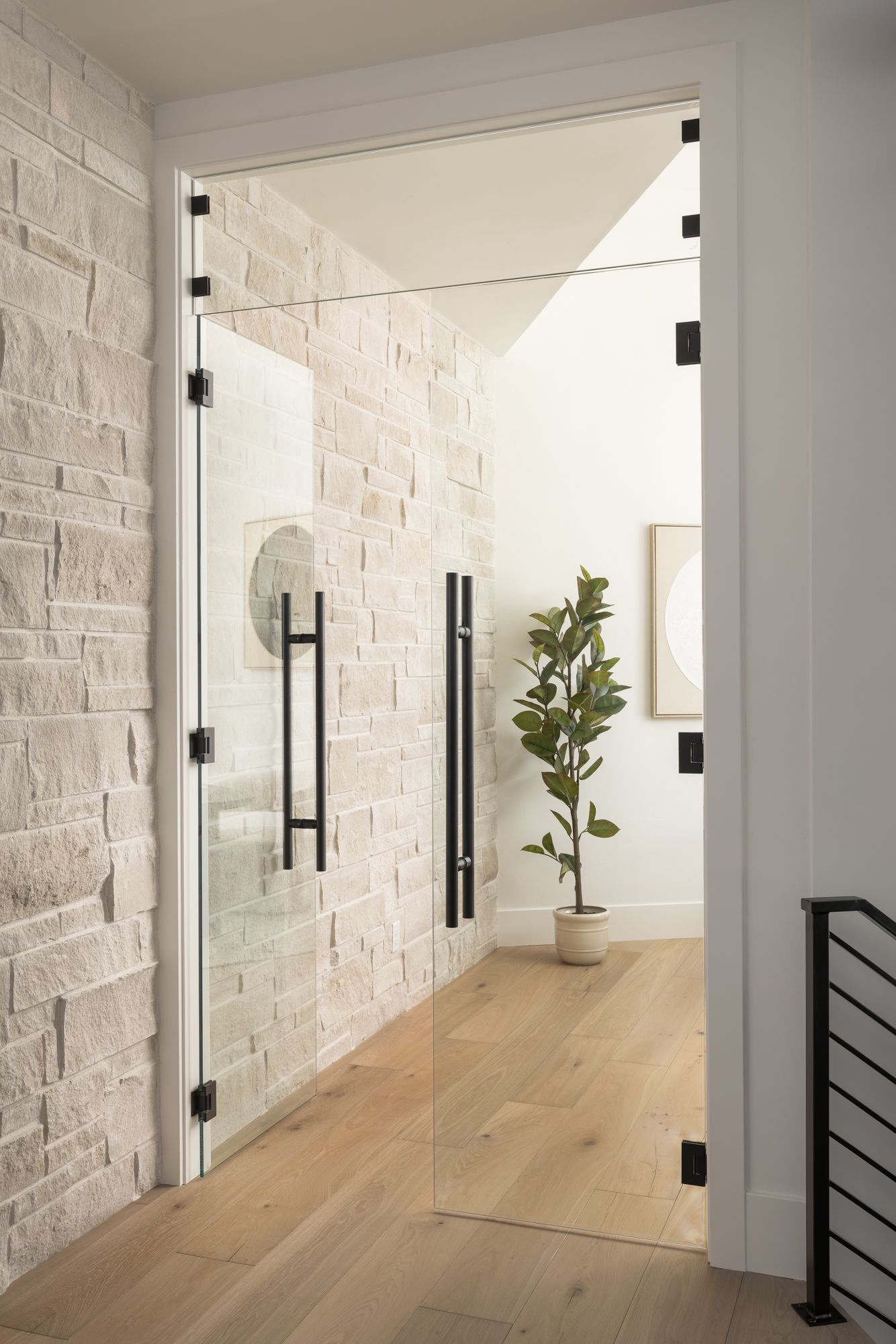 Modern entryway with glass doors, light wood floors, white brick wall, and potted plant