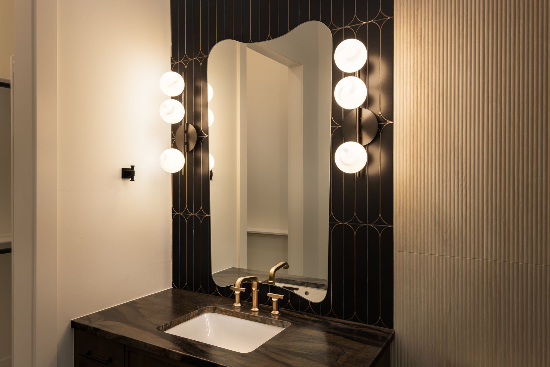 Modern vanity with round lights, tall mirror, black countertop, and striped wall paneling