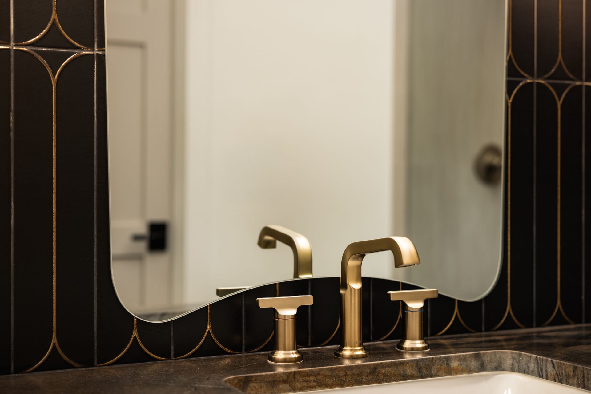Modern bathroom vanity with brass faucets, mirror, and dark decorative tile accents