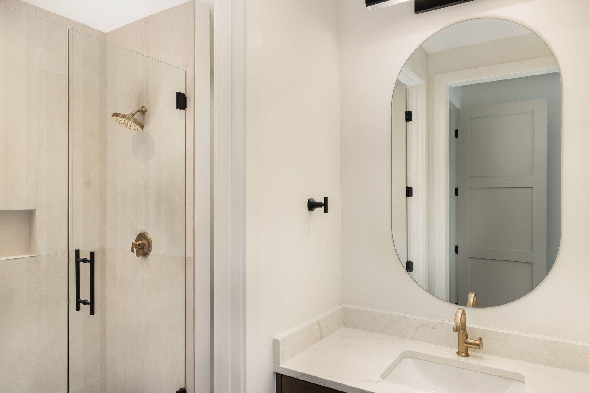 Bright bathroom vanity with oval mirror and glass shower with brass fixtures