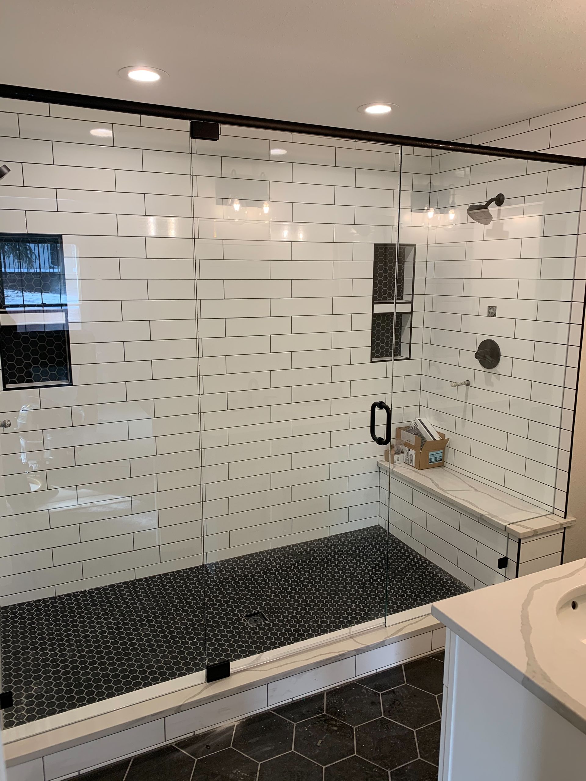 Modern bathroom with white subway tile shower, black floor, and built-in bench seat