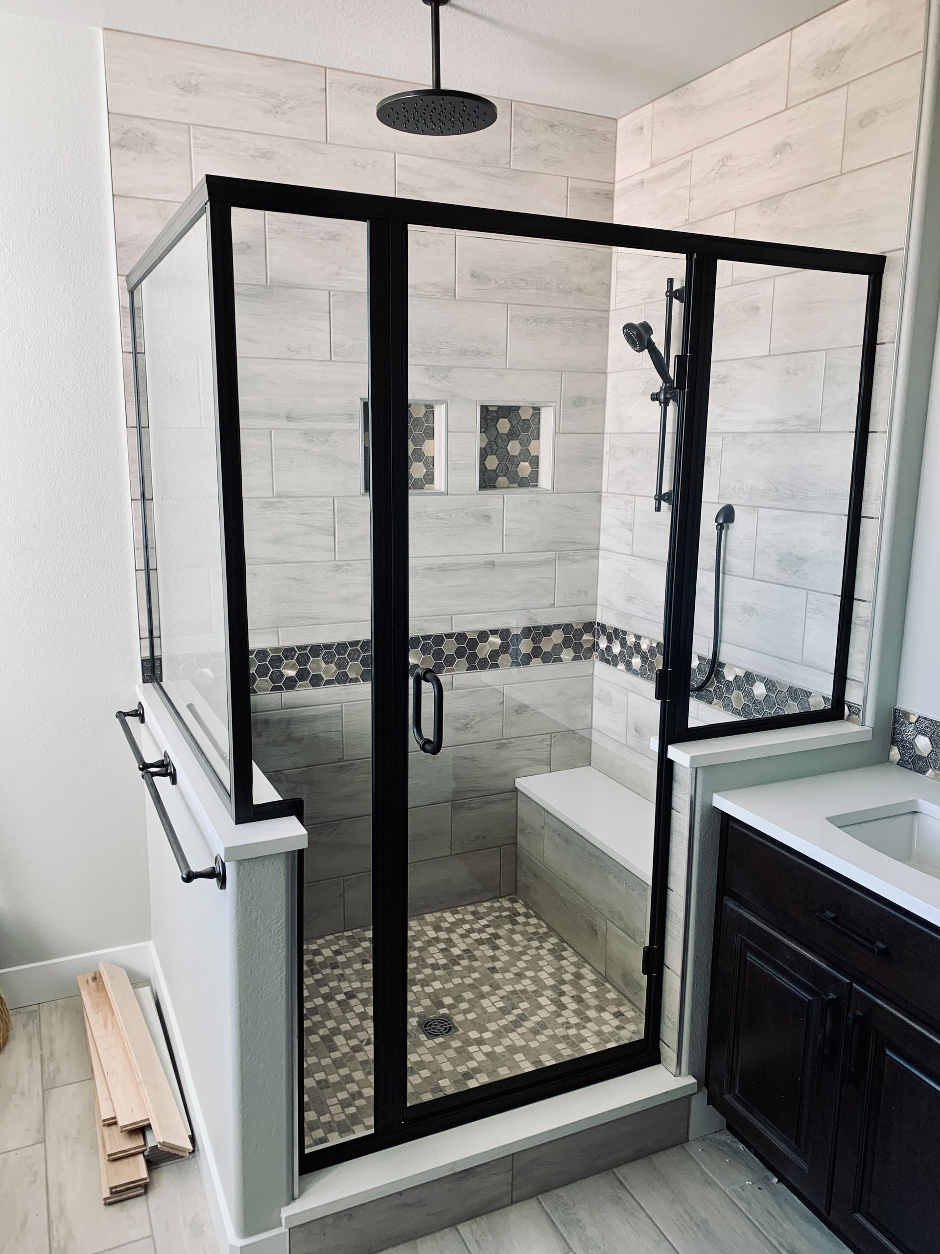Black-framed glass shower with white tile and mosaic floor in a bathroom