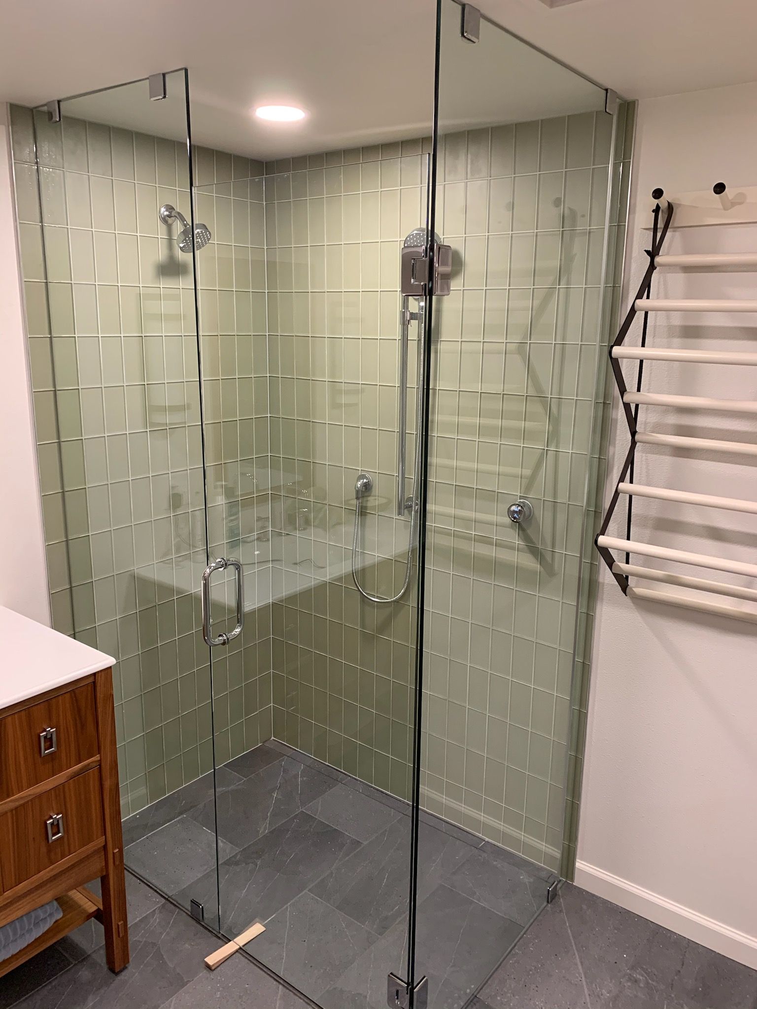 Glass shower enclosure with green tile walls in a modern bathroom