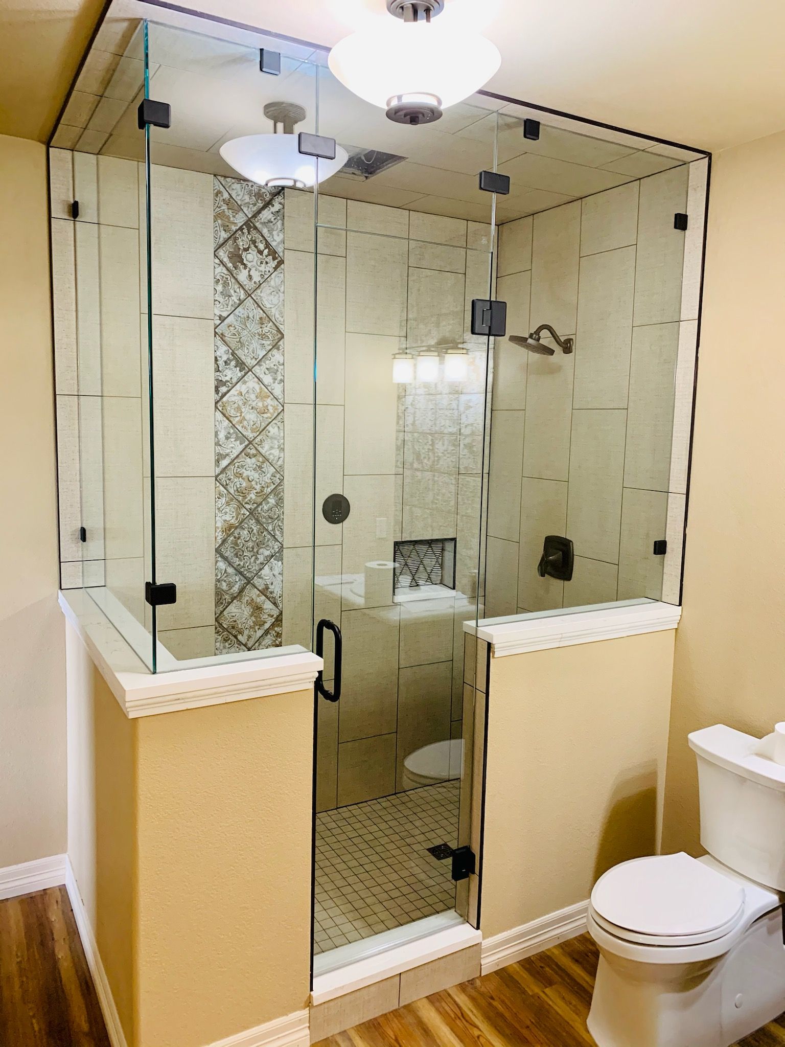 Glass-enclosed shower and toilet in a beige bathroom with decorative tile accents.
