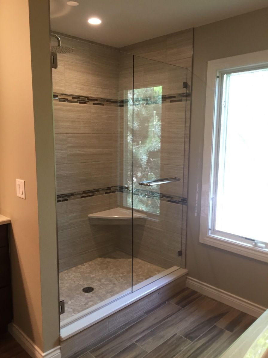 Glass walk-in shower with tiled walls, mosaic accent strip, corner shelf, and window beside it