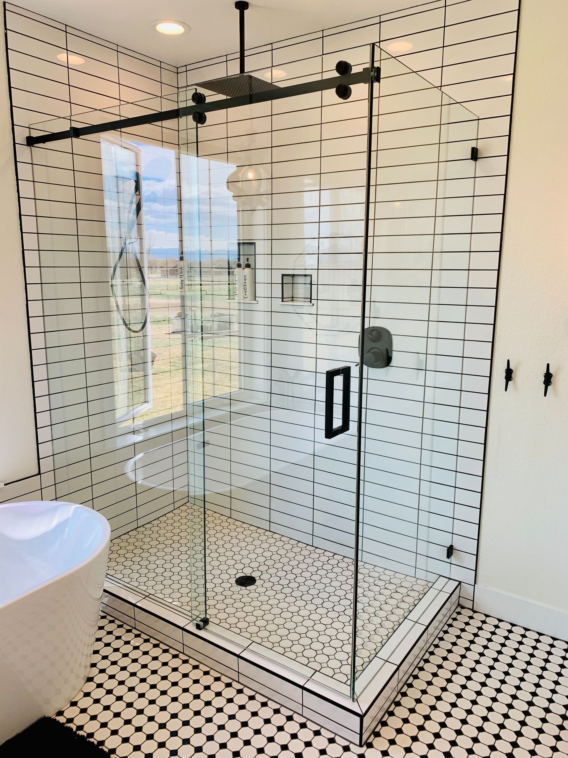 Modern bathroom with glass shower enclosure, black hardware, and white patterned tile walls and floor