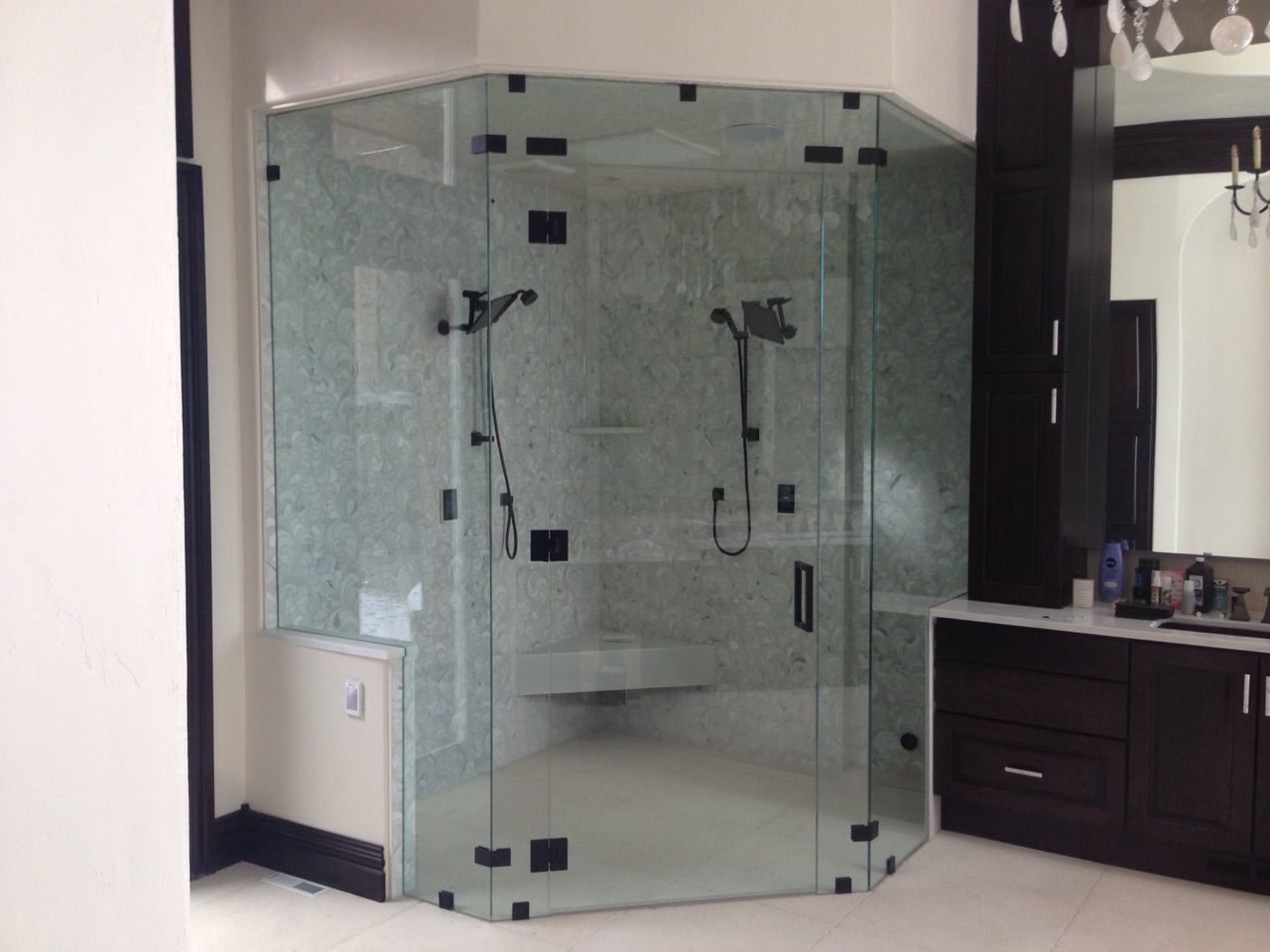 Glass shower stall in a modern bathroom with green tile and dark wood vanity.
