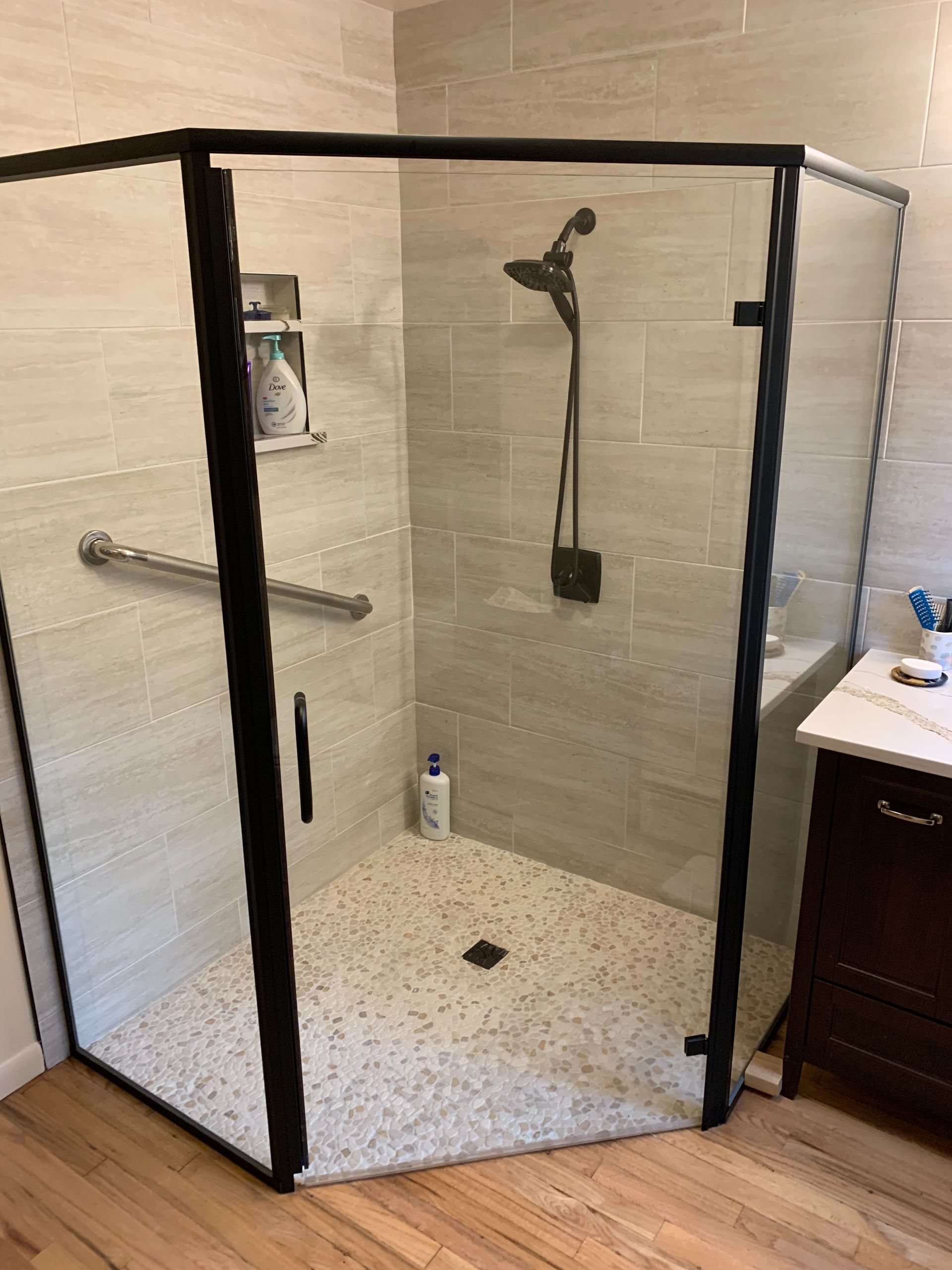 Accessible walk-in shower with black-framed glass doors, gray tile walls, and a handheld showerhead.
