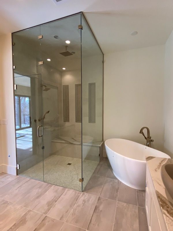 Modern bathroom with glass shower enclosure, freestanding tub, and light wood tile floor