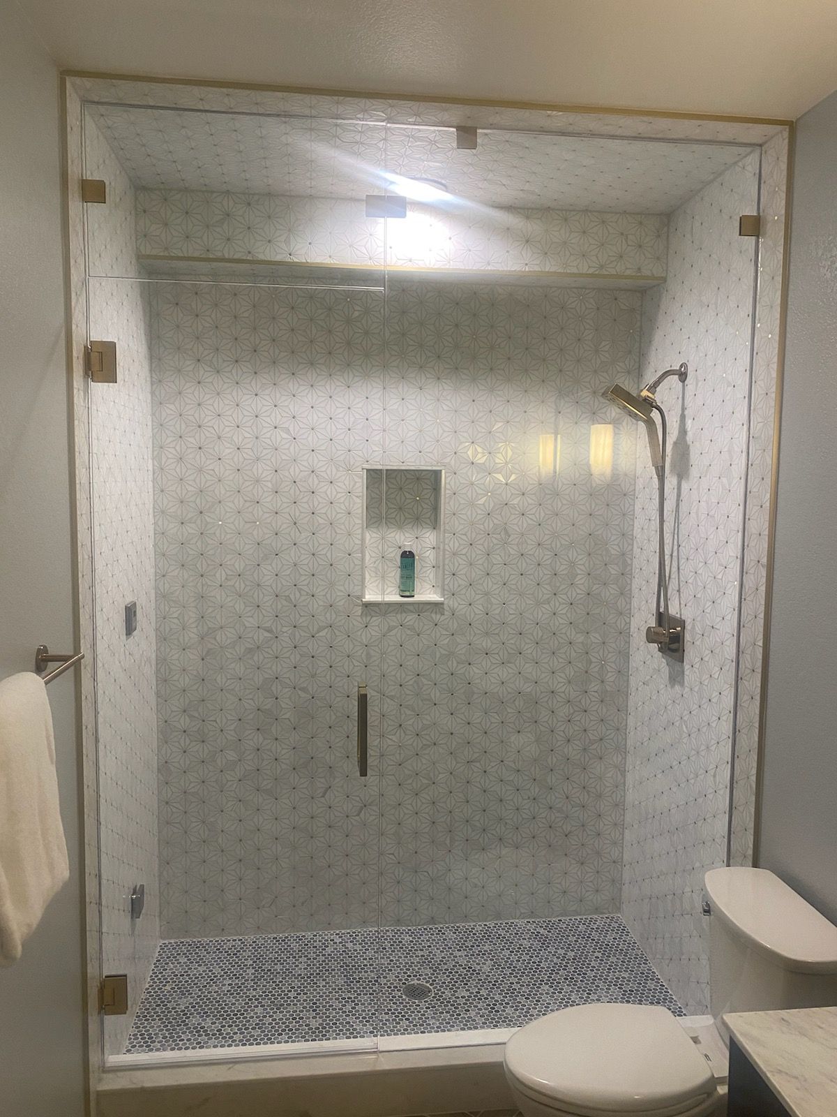 Glass shower stall with patterned tile walls, white bench, and blue mosaic floor