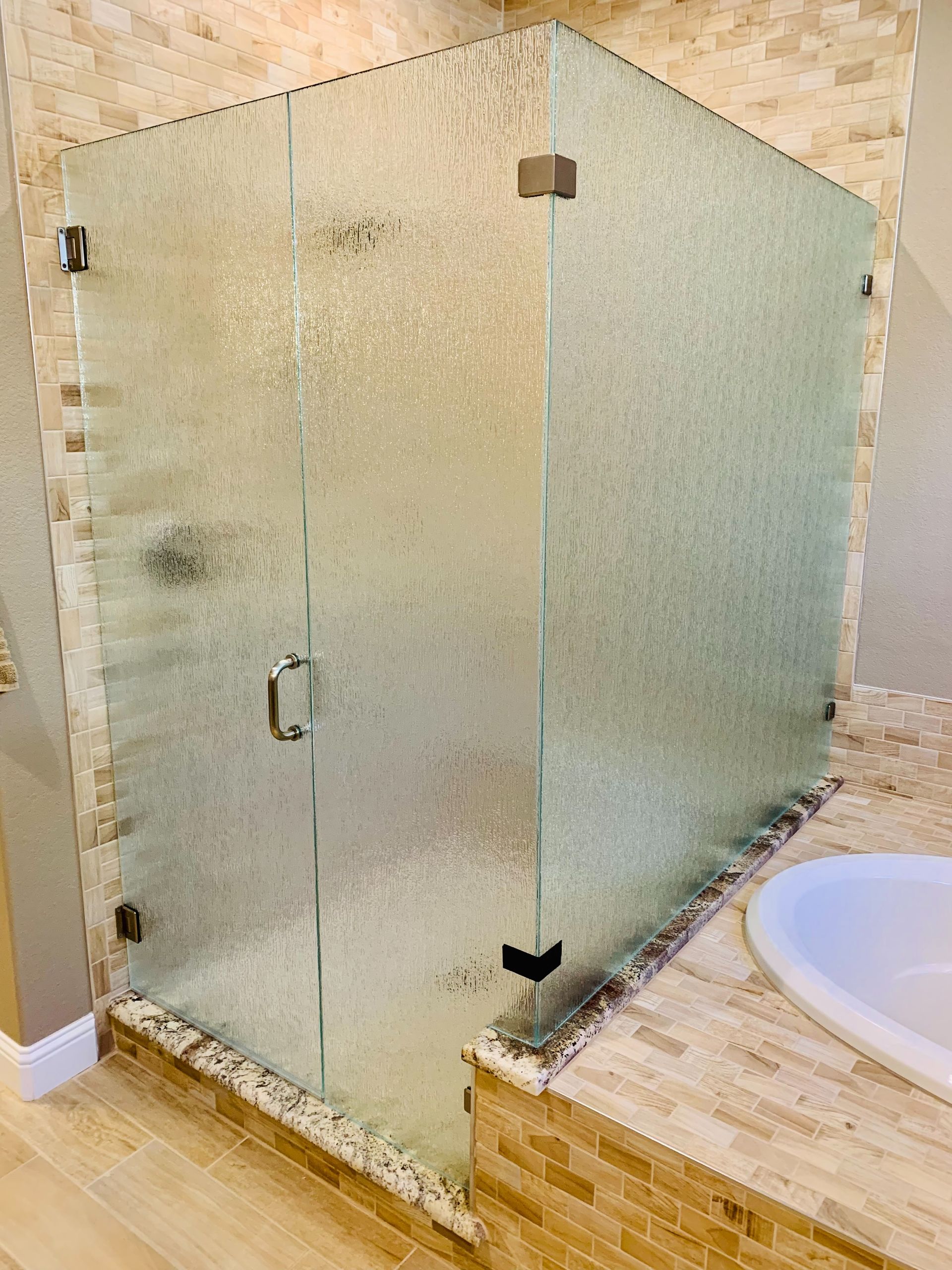 Frameless frosted glass corner shower with beige tile and a stone bathroom floor