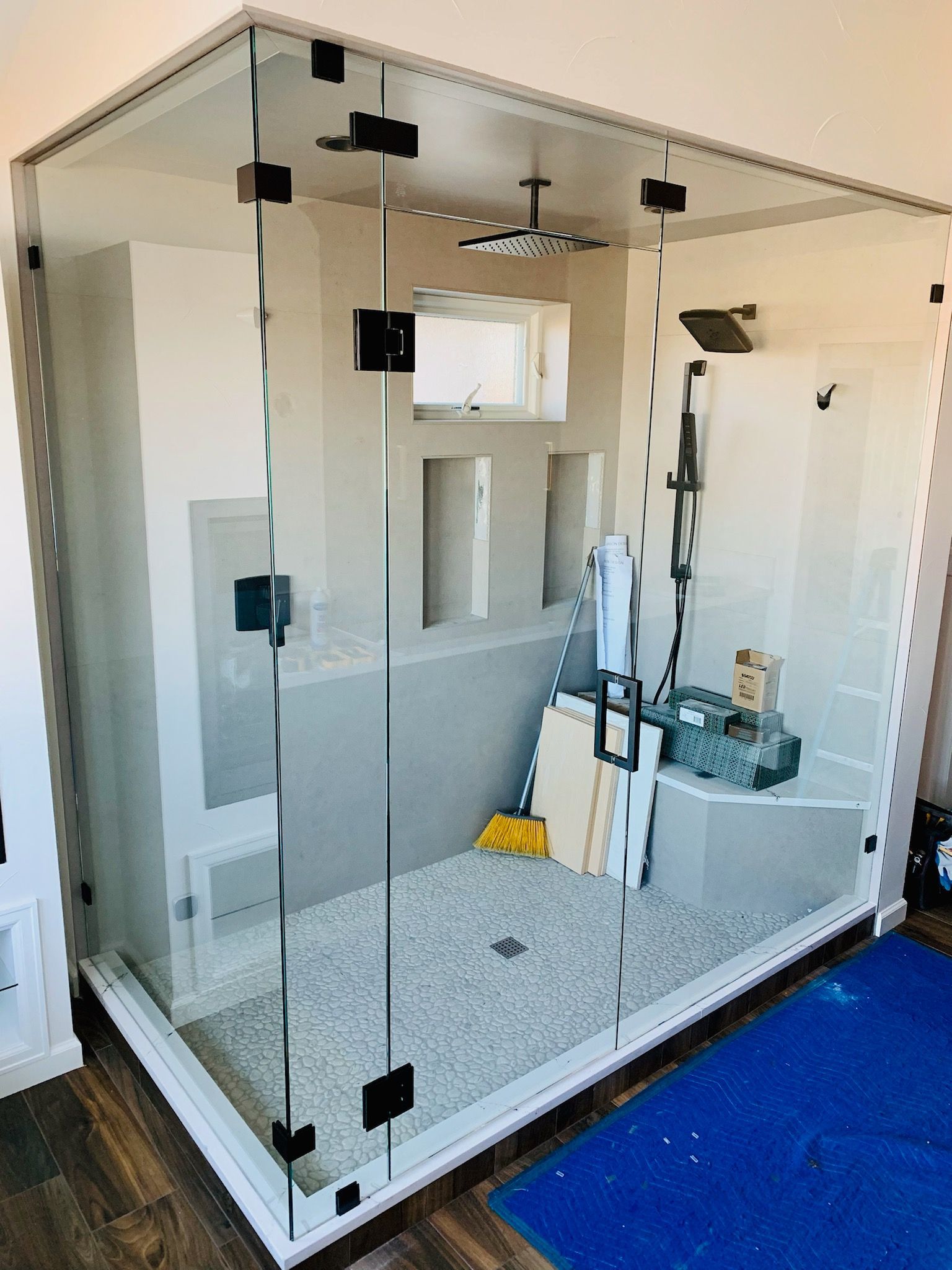 Glass shower enclosure with black hardware and gray tile floor, seen in a bathroom.